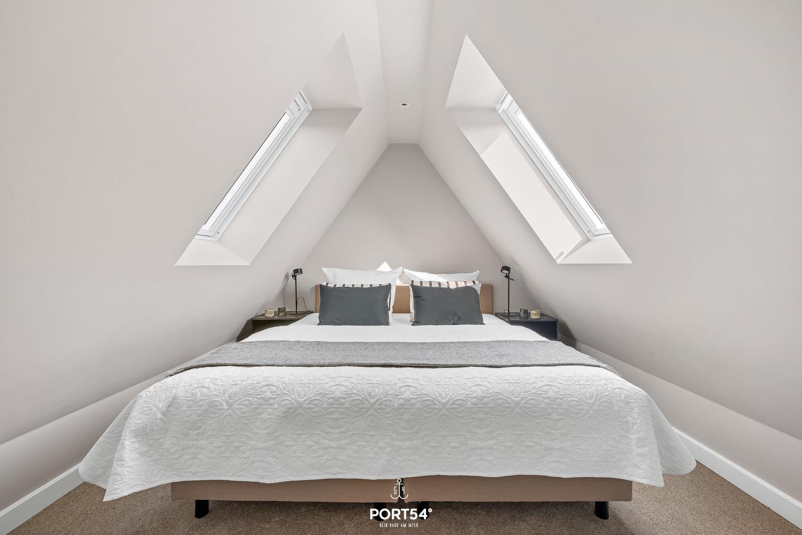 Schlafzimmer mit Dachfenstern und Bett mit grauen Kissen.