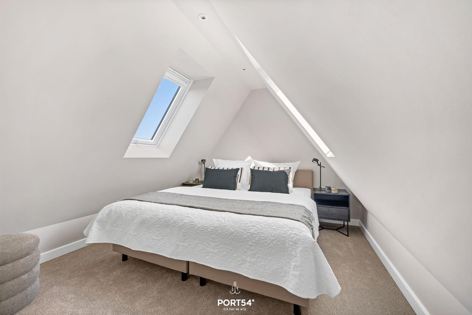 Schlafzimmer mit Dachschrägen, Dachfenster und Bett mit Kissen.