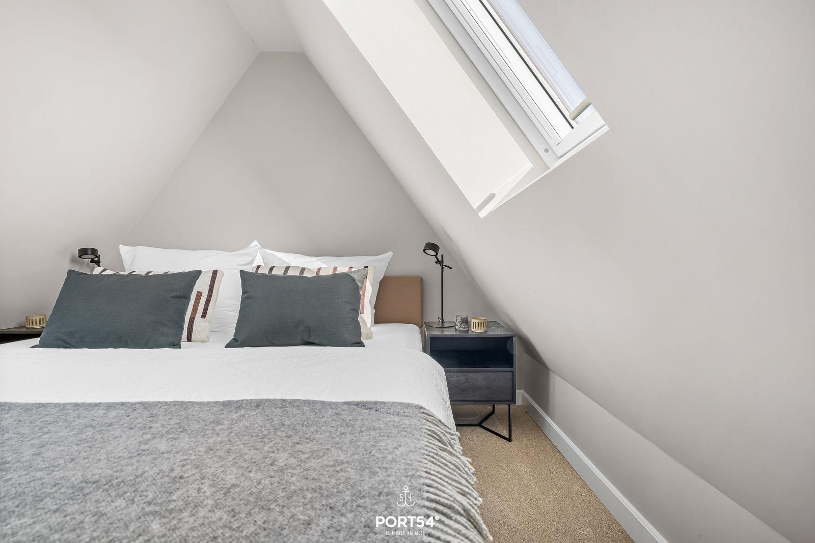 Schlafzimmer mit Dachschrägen, Dachfenster, Bett und Nachttisch.