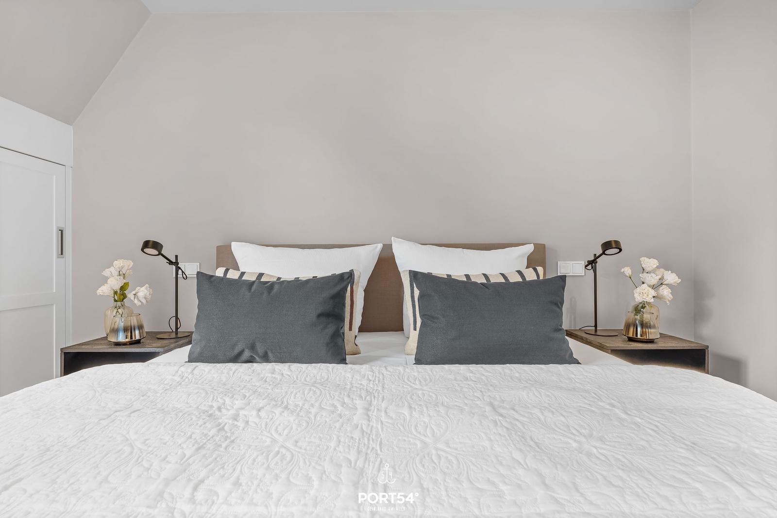 Schlafzimmer mit Bett, Nachttischen und Blumen.