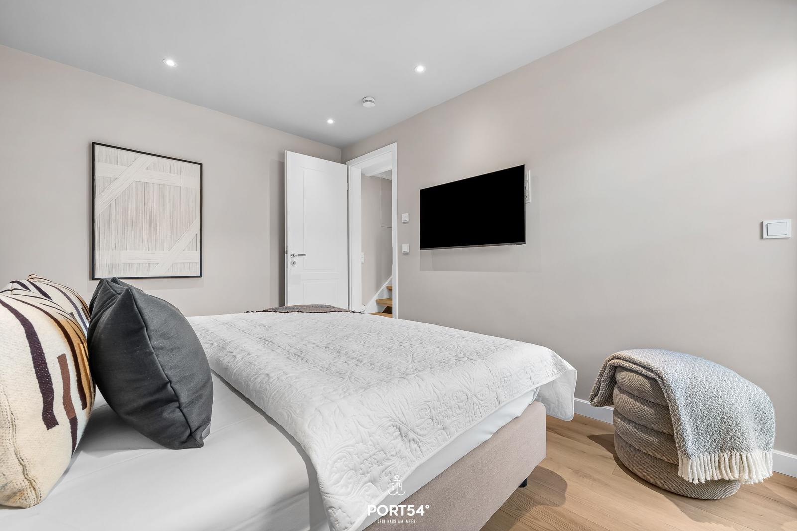 Schlafzimmer mit Bett, Wandbild, TV und Sitzhocker.