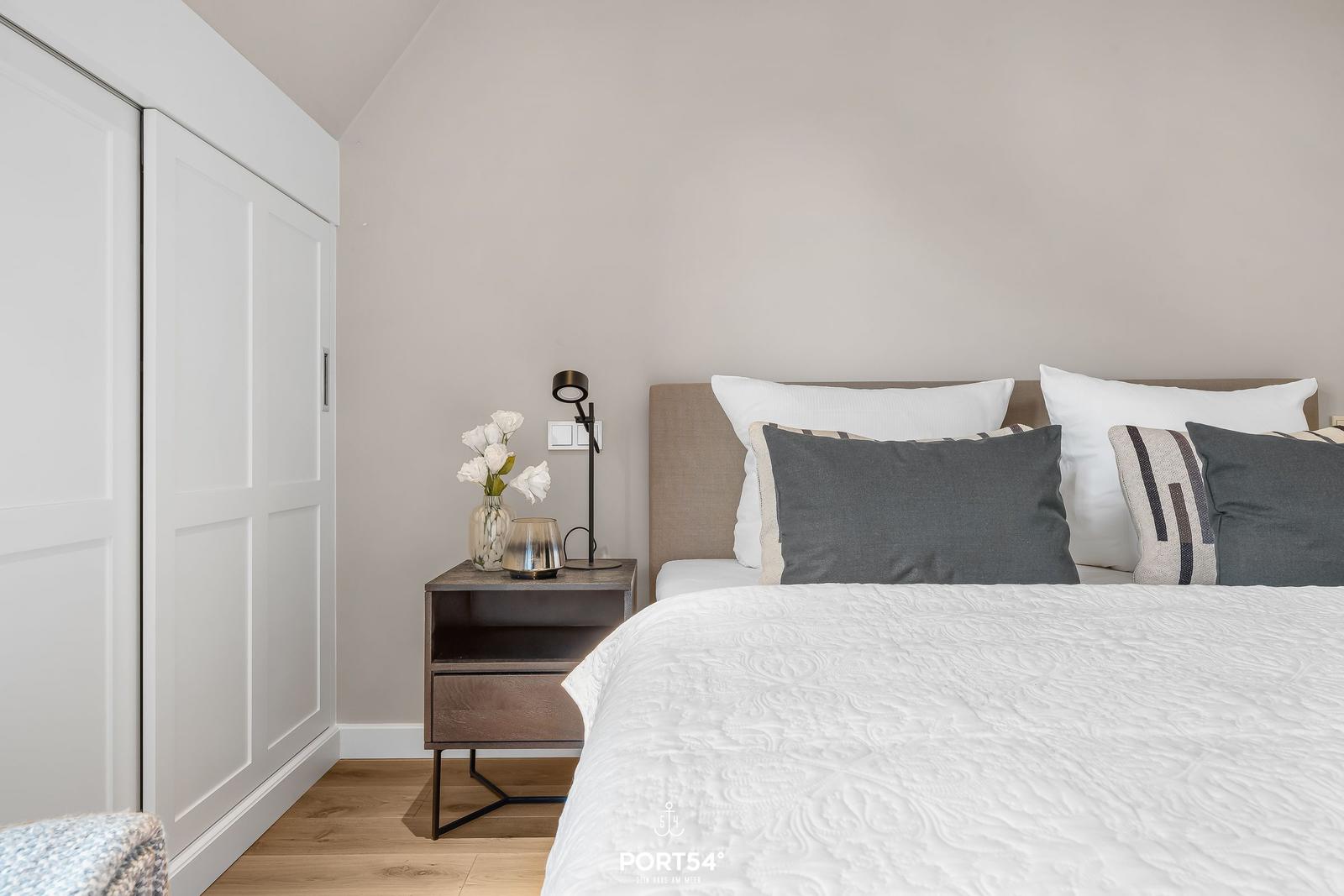 Schlafzimmer mit Bett, Nachttisch und Schrank. Wandfarbe beige, Boden aus Holz.