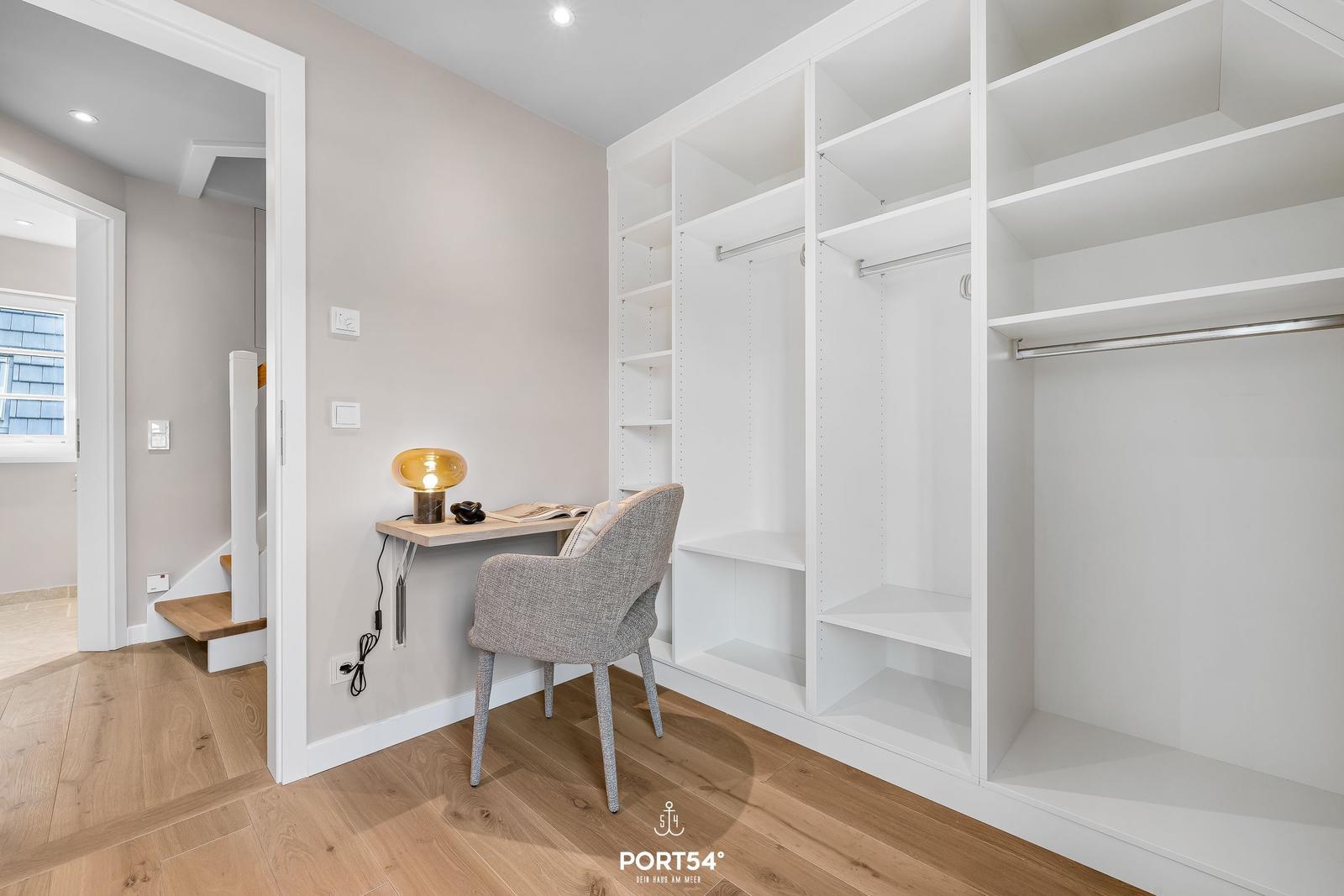 Schlafzimmer mit Kleiderschrank und Schreibtisch mit Stuhl und Lampe.