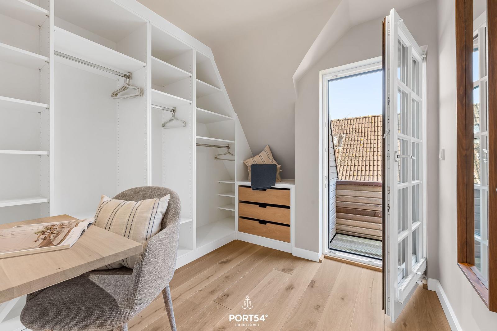 Schlafzimmer mit Kleiderschrank, Schreibtisch und Balkontür.
