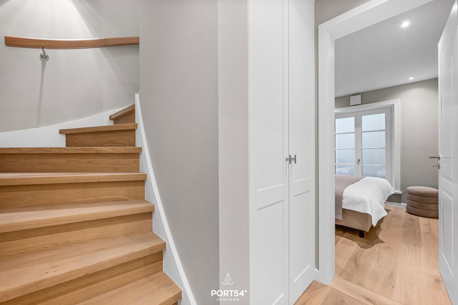 Holztreppe führt zur Schlafzimmer-Ecke mit Bett und Fenster.