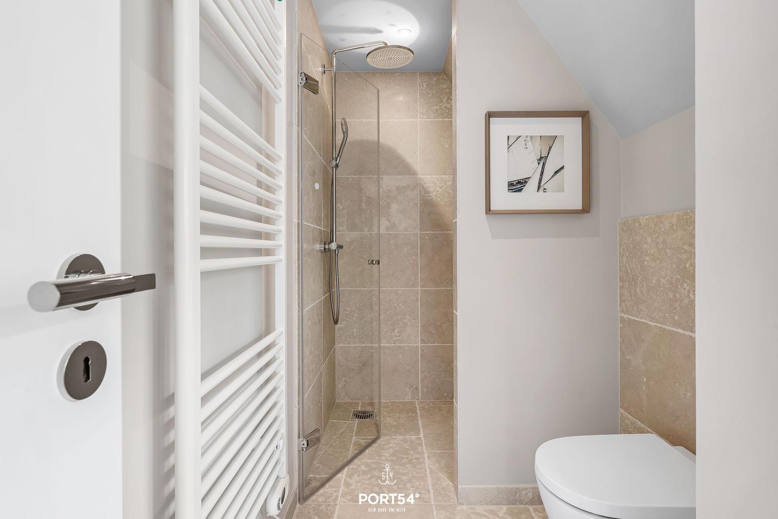 Dusche mit Glaswand, Toilette und Heizung an der Wand