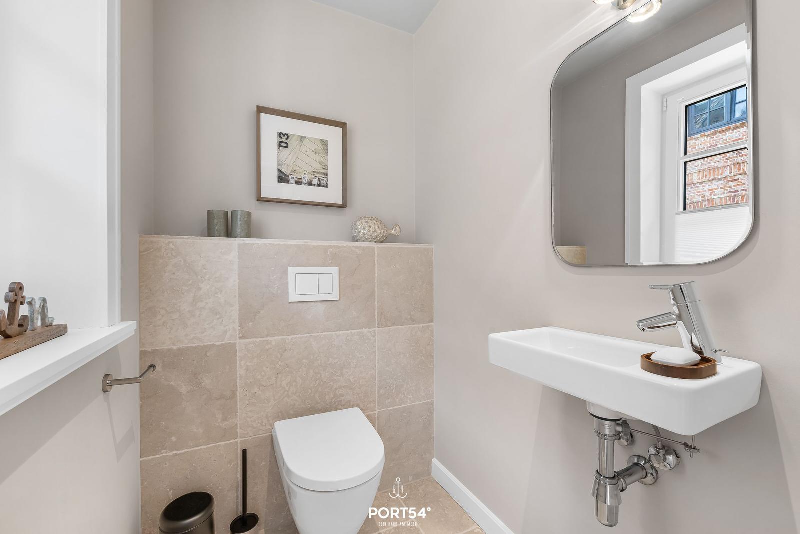 Badezimmer mit Toilette, Waschbecken und Spiegel. Wandverkleidung aus Stein.