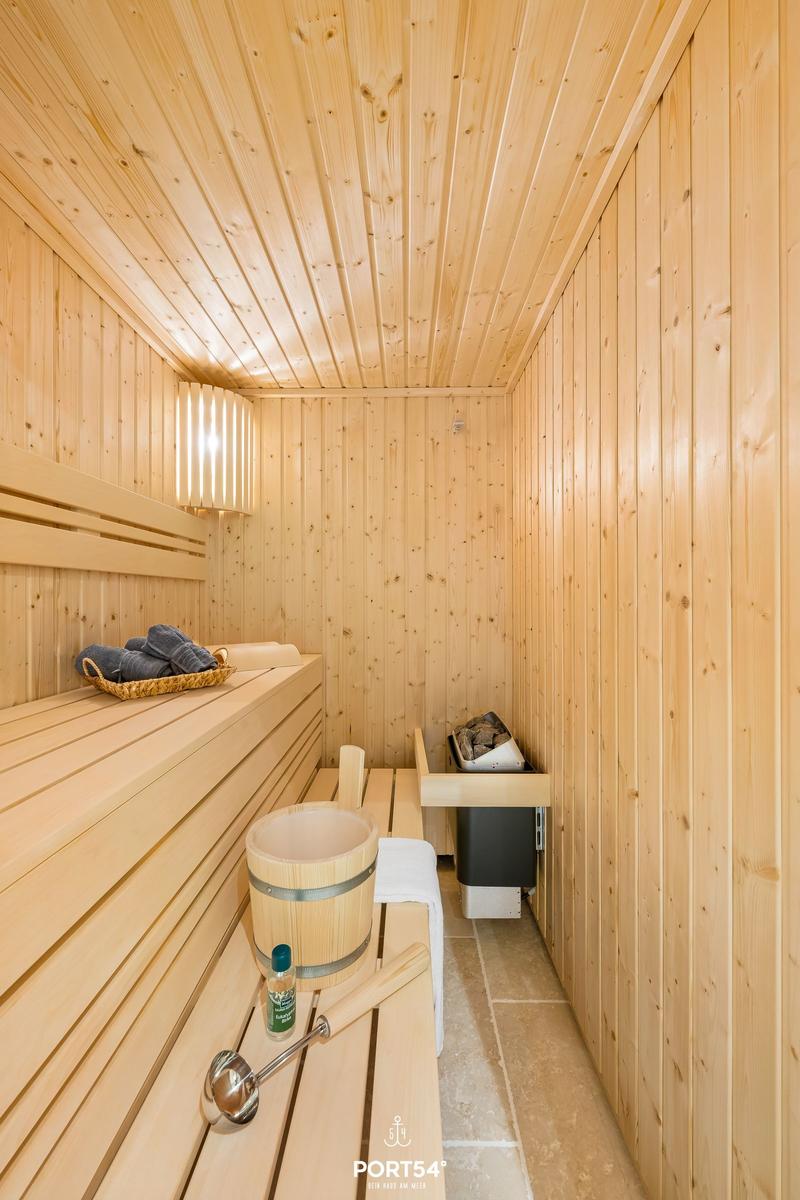 Sauna mit Holzbank, Eimer, Korb und Heizung.