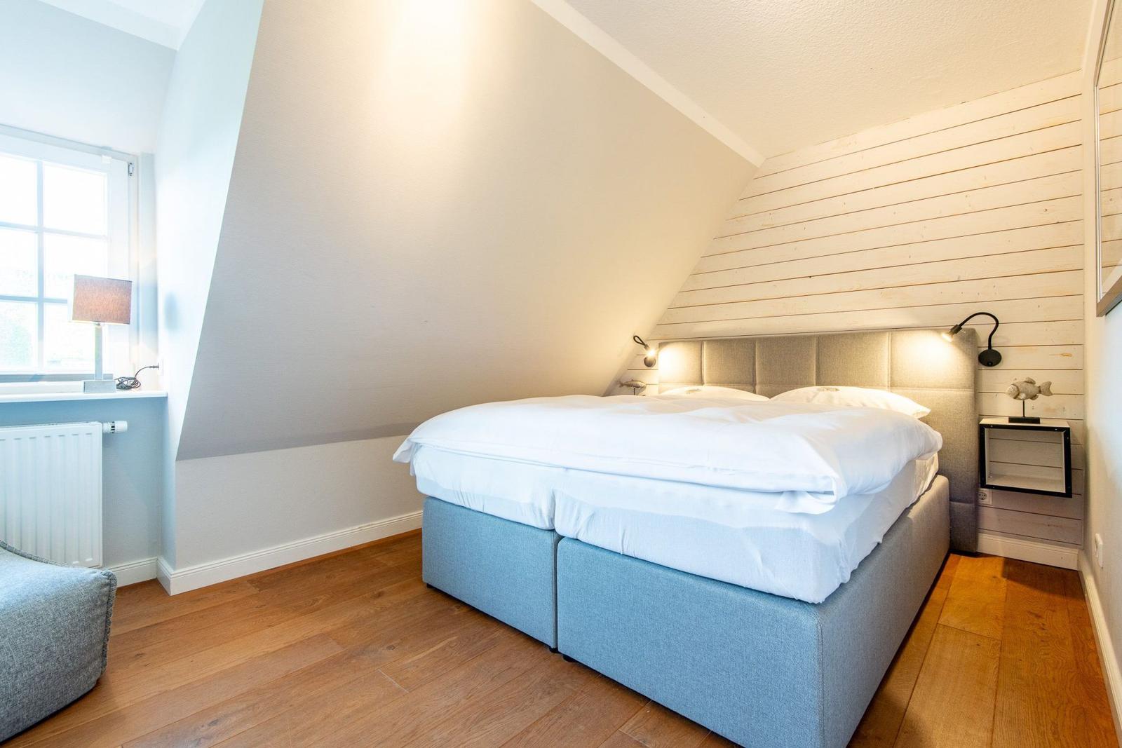 Schlafzimmer mit Doppelbett, Holzboden und Holzwand. Fenster mit Tischlampe.