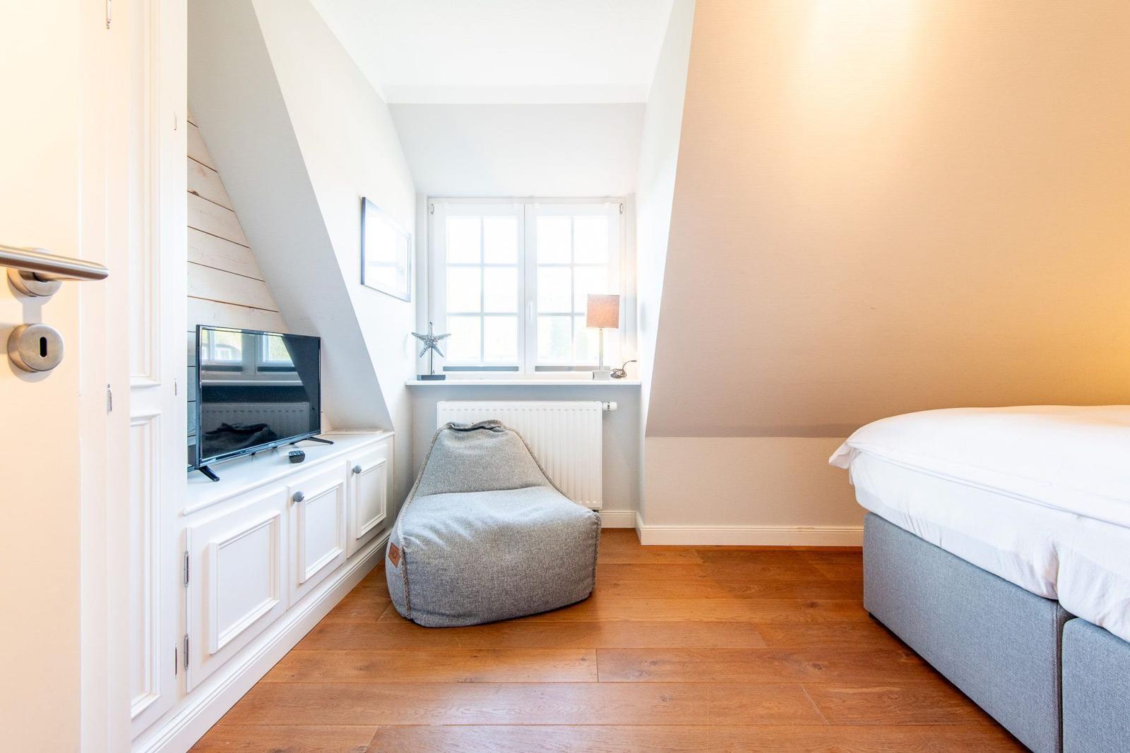 Schlafzimmer mit Bett, Sitzgelegenheit und TV-Anlage unter Dachschrägen.