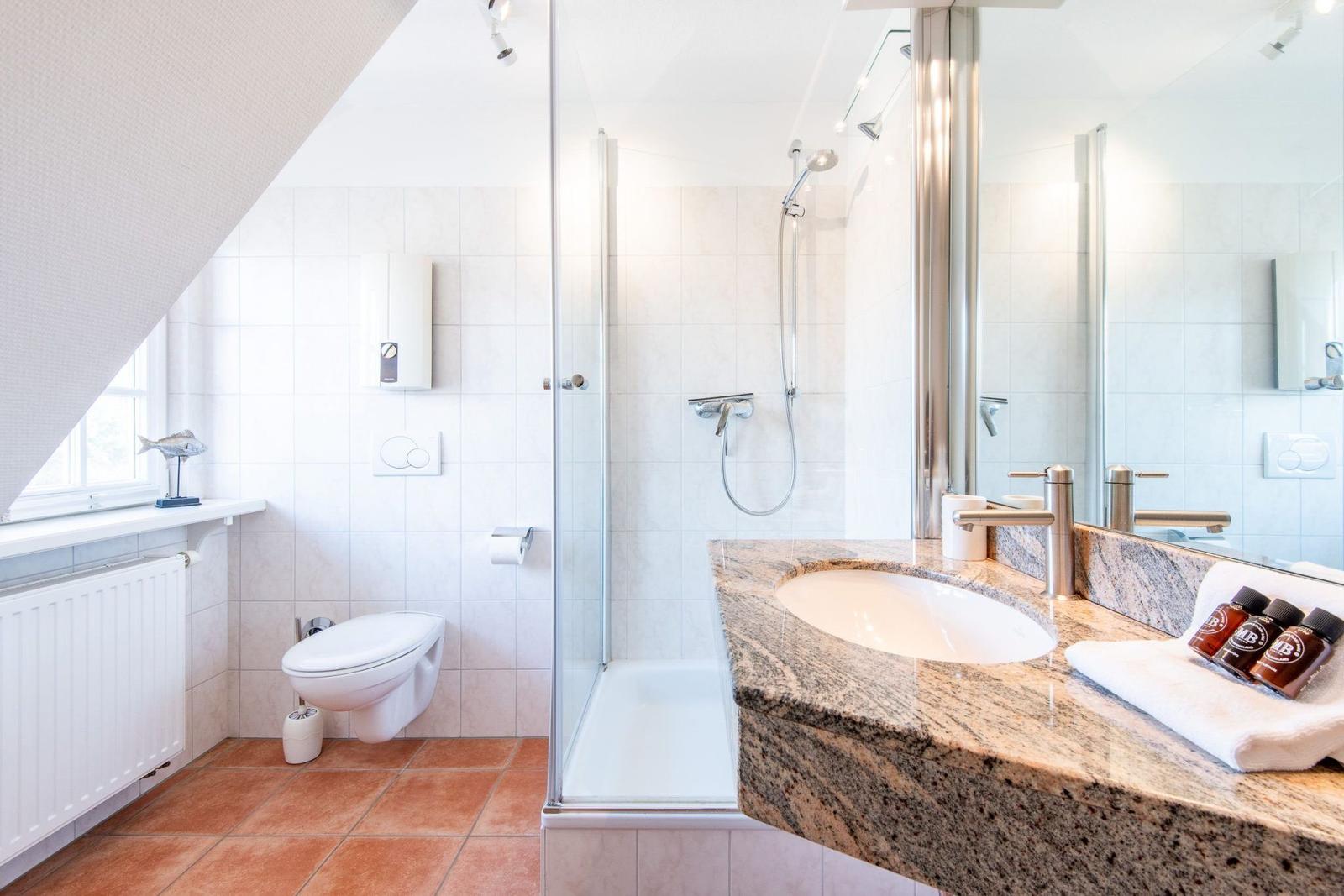 Badezimmer mit Dusche, Waschbecken und Toilette unter Dachschräge.