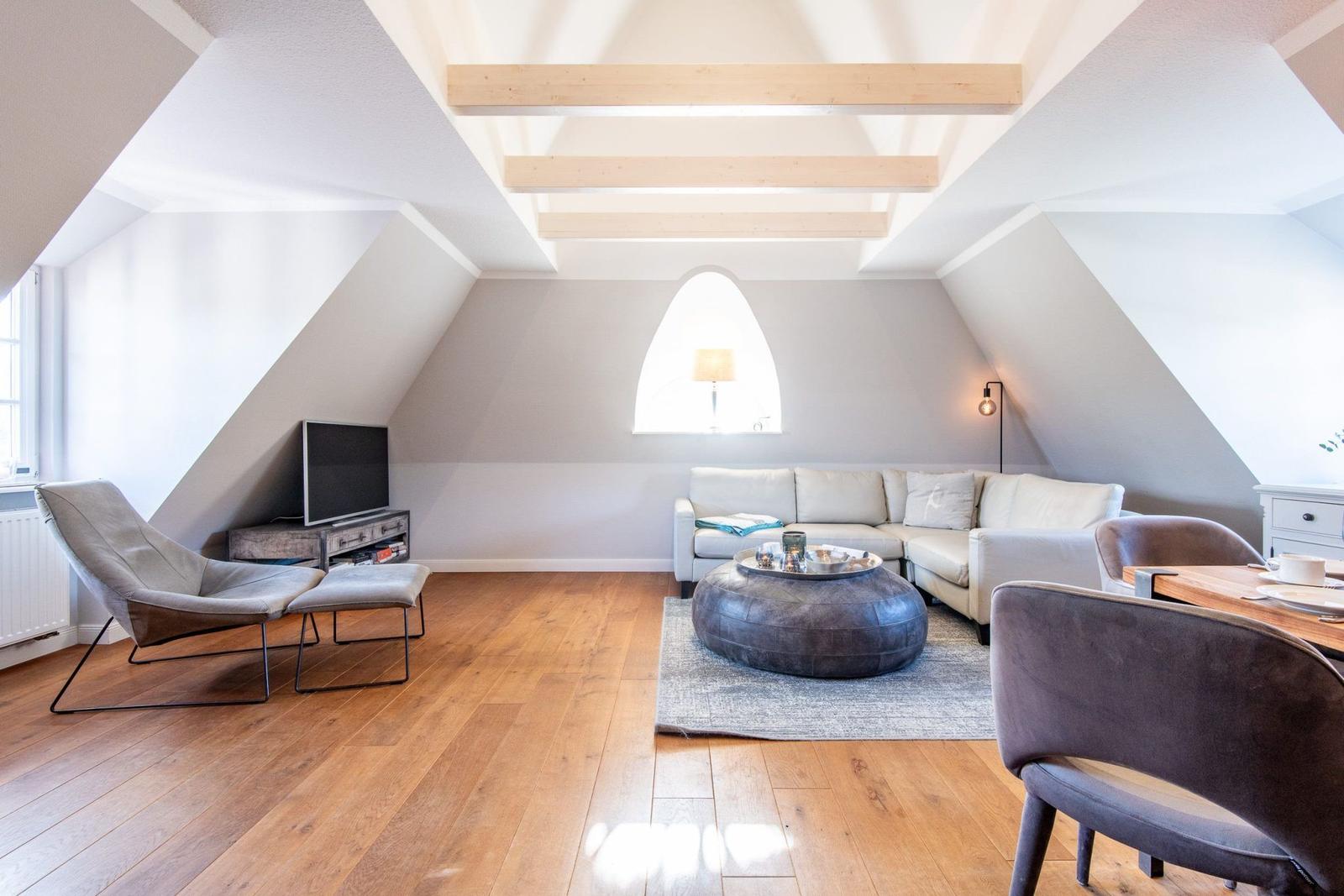Wohnraum mit Holzboden, Sofa, Sessel und runden Tisch unter Holzbalkendecke.