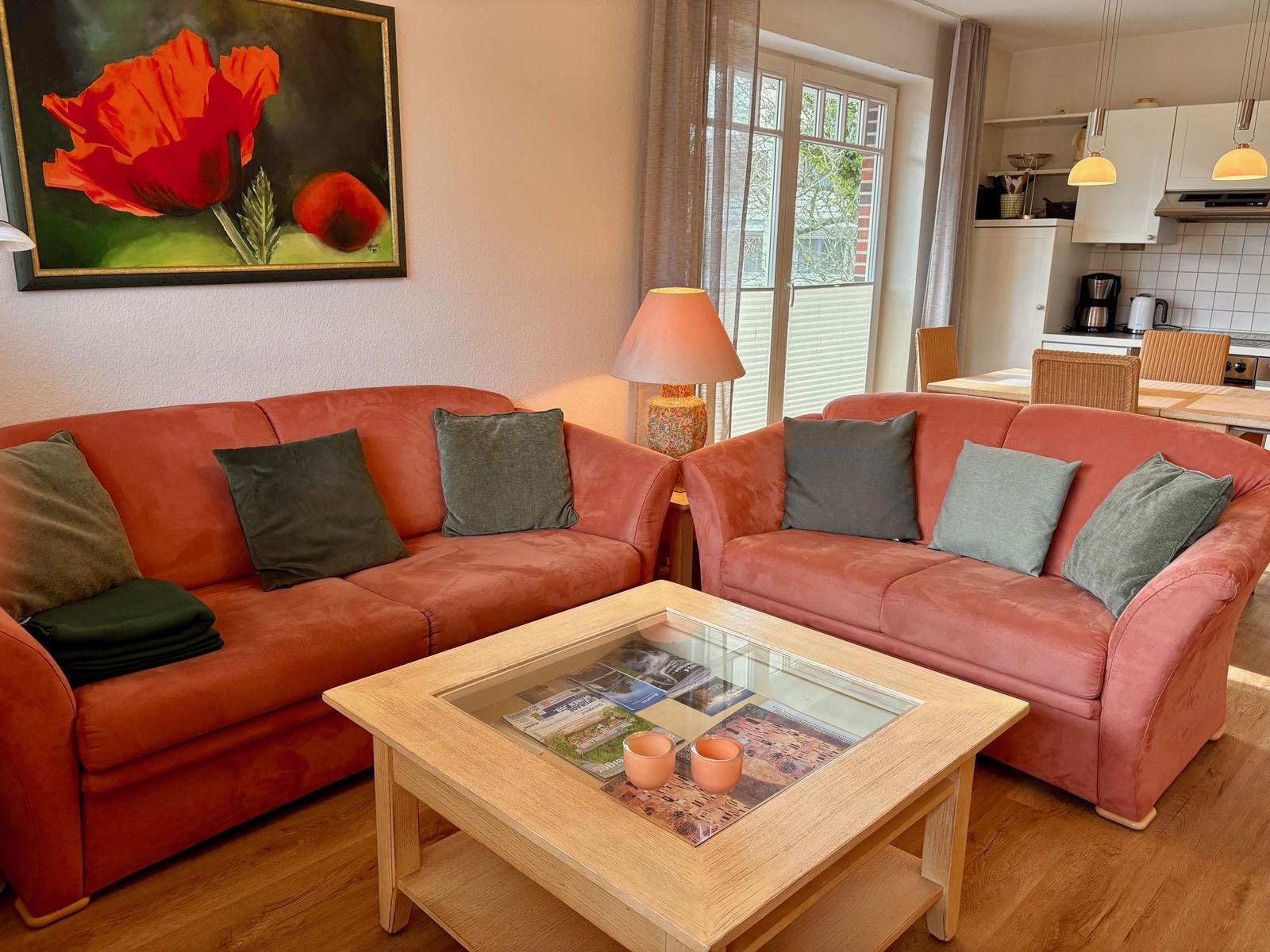 Zwei orangefarbene Sofas mit Kissen um einen Holztisch mit Glasplatte.