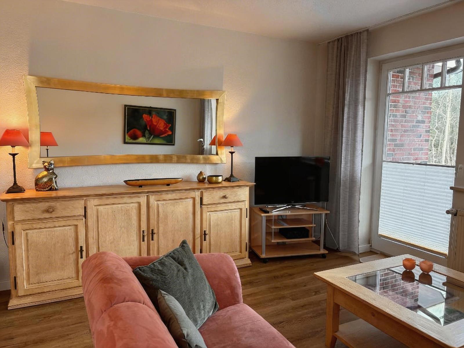 Ein Wohnzimmer mit einem Sofa, einem TV und einem Sideboard mit Spiegel.