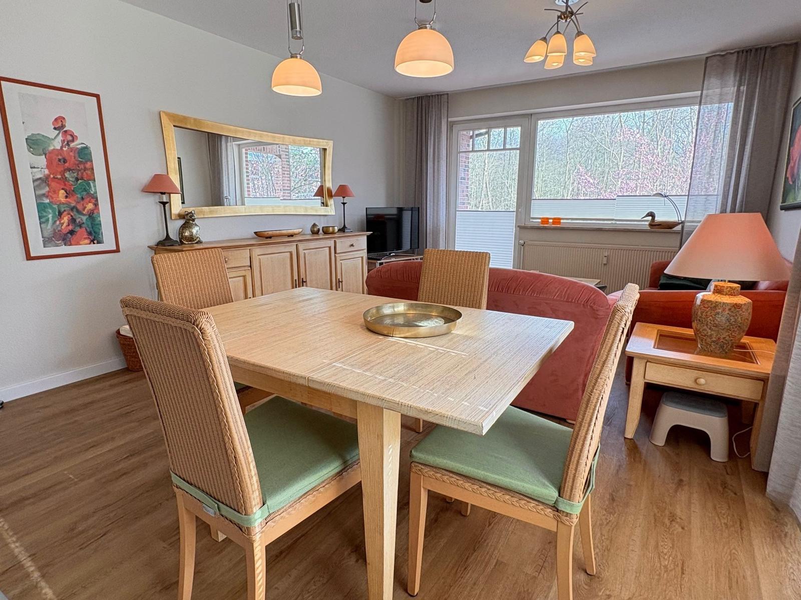 Essbereich mit Holztisch, Stühlen und rotem Sofa. Fenster mit Blick auf Bäume.