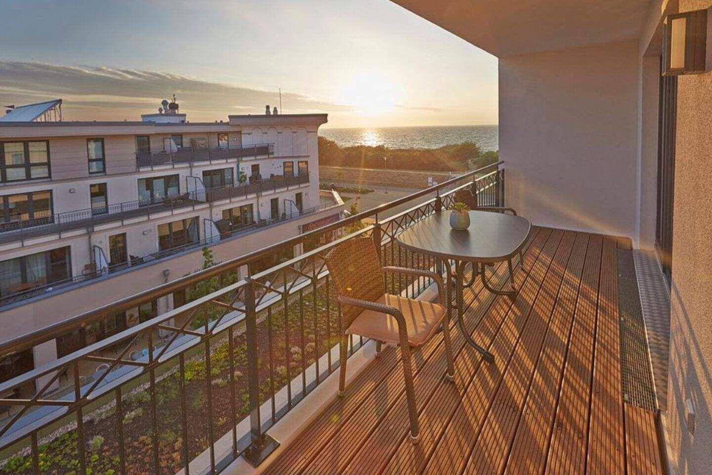 Terrasse mit Tisch und Stühlen, Blick auf Meer und Gebäude.