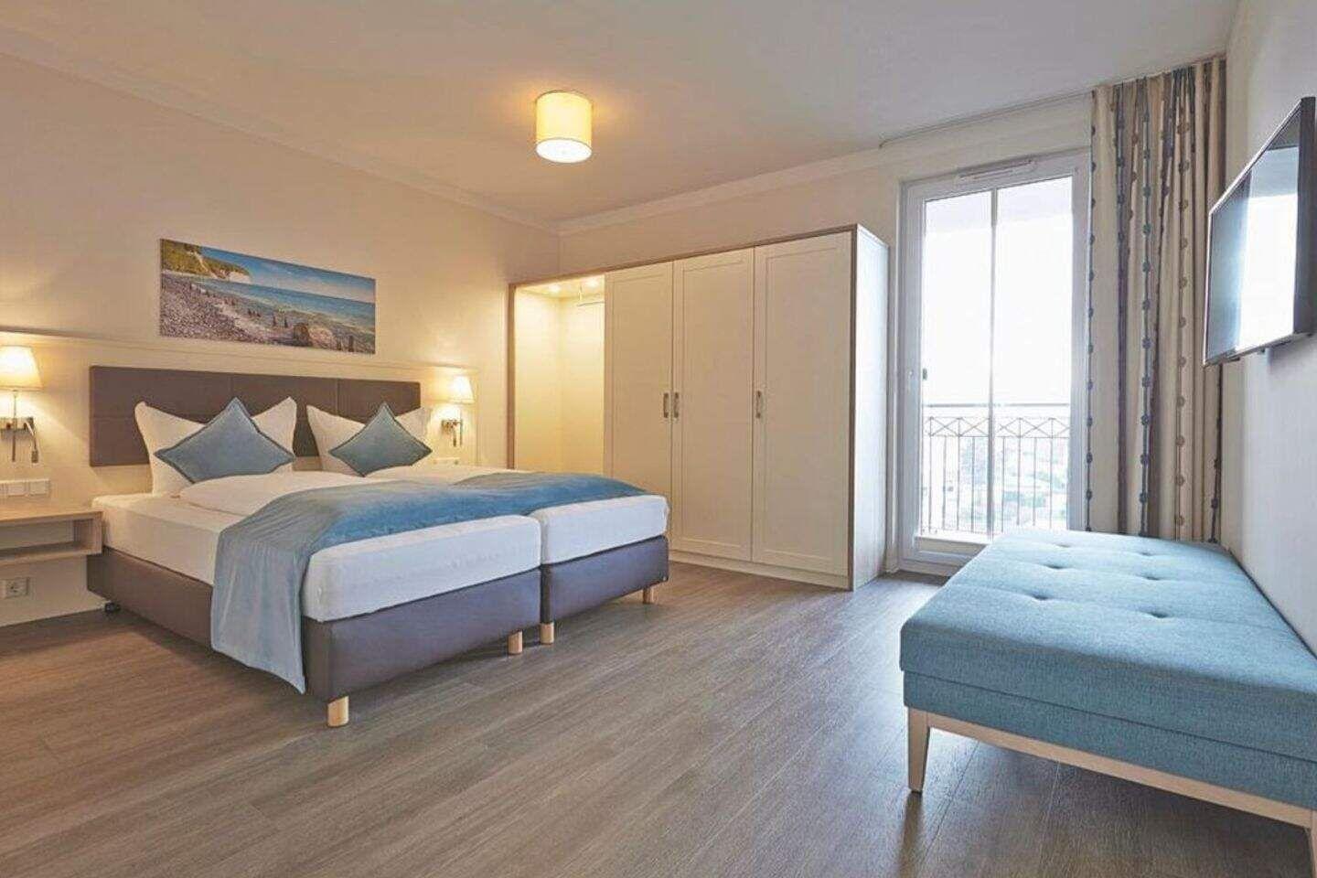 Zimmer mit Doppelbett, Kleiderschrank, TV und Balkonzugang.