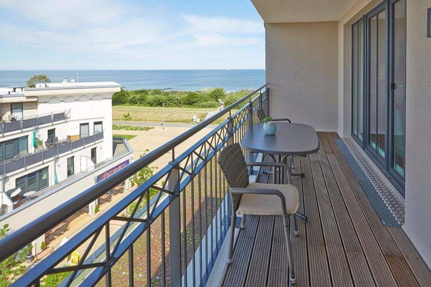 Terrasse mit Tisch und Stühlen, Blick auf Meer und Gebäude.