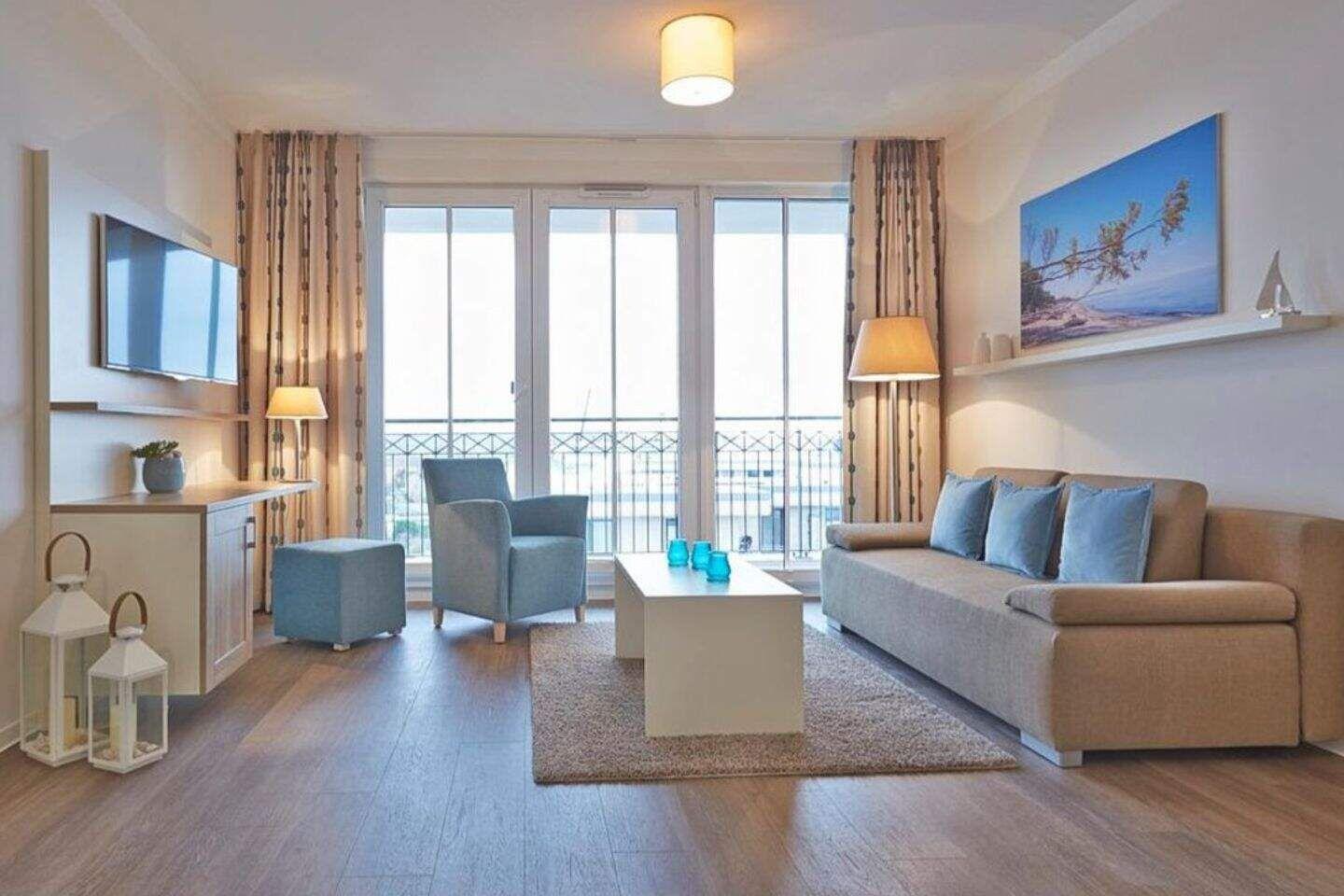 Wohnzimmer mit Sofa, Sessel und TV. Balkon mit Blick auf Wasser.