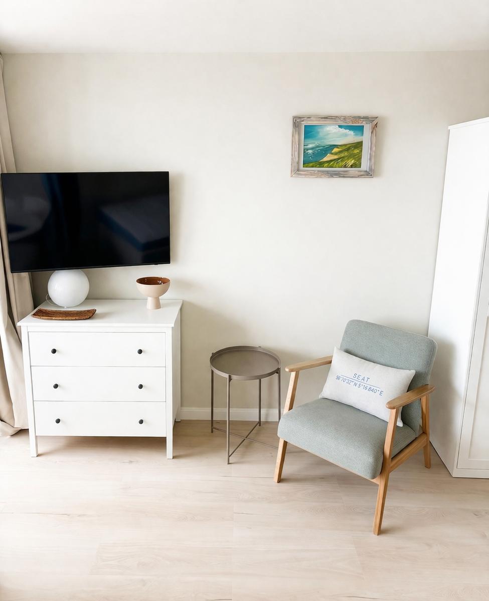 Ein Raum mit Fernseher, Schrank, Stuhl und Bild an der Wand.