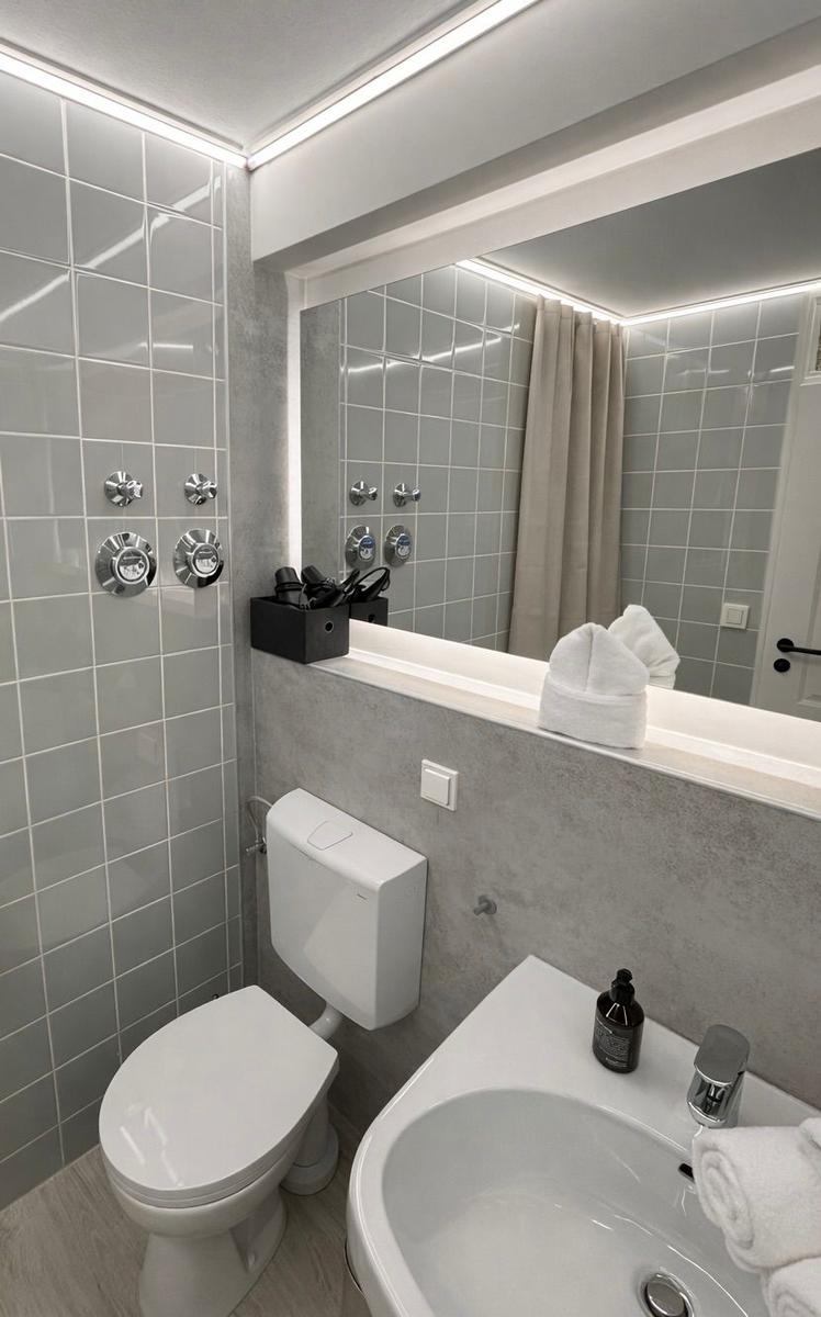 Badezimmer mit Toilette, Waschbecken und Dusche mit grauen Fliesen.