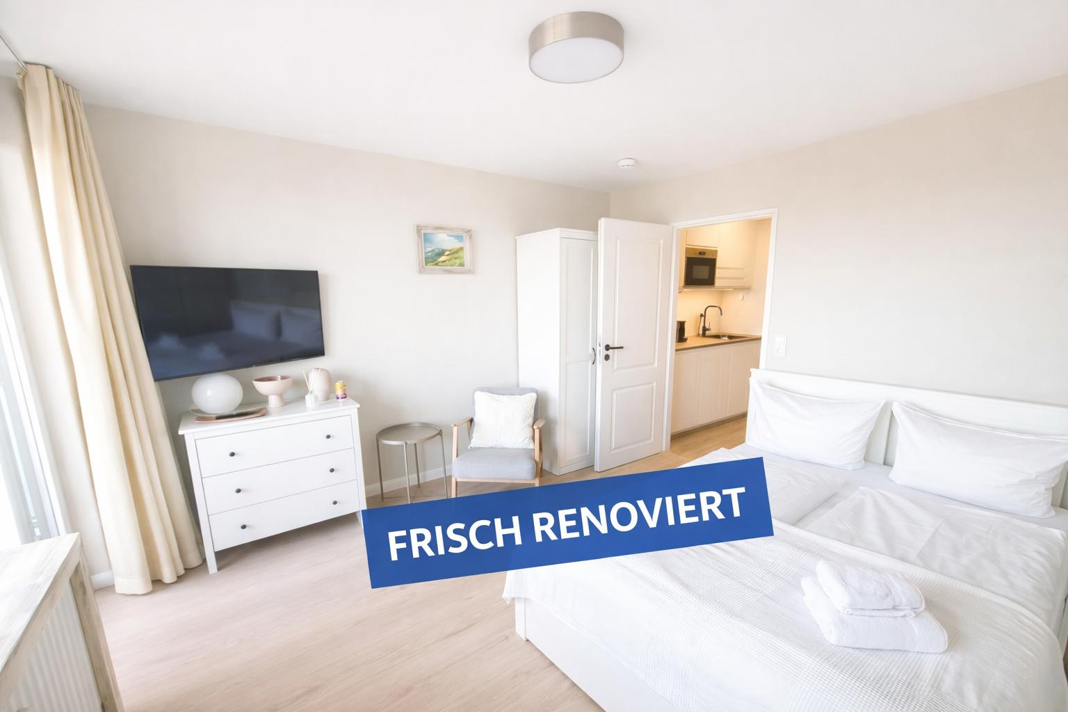 Frisch renoviertes Schlafzimmer mit Bett, TV und Blick in die Küche.