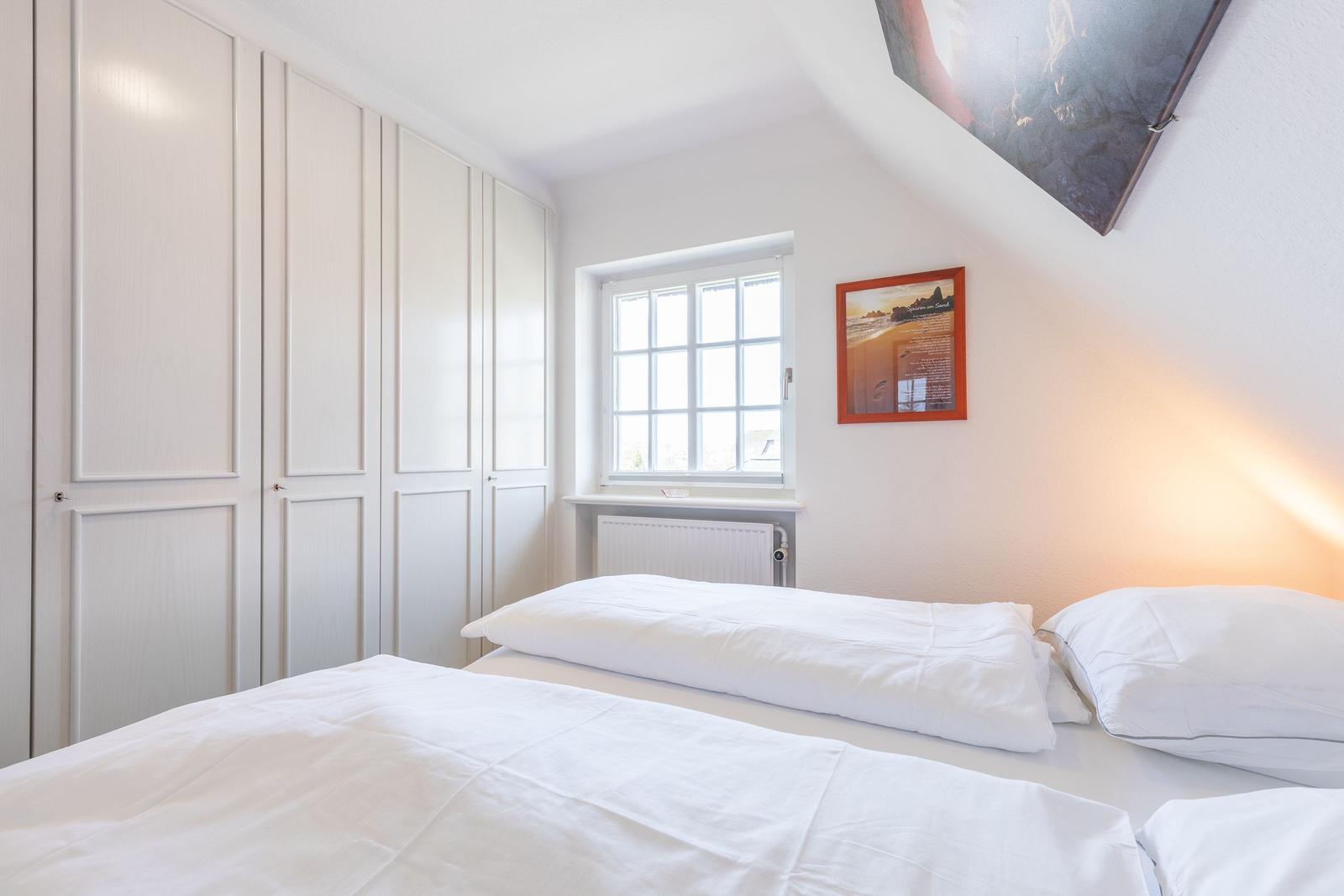 Schlafzimmer mit Bett, Kleiderschrank und Fenster.