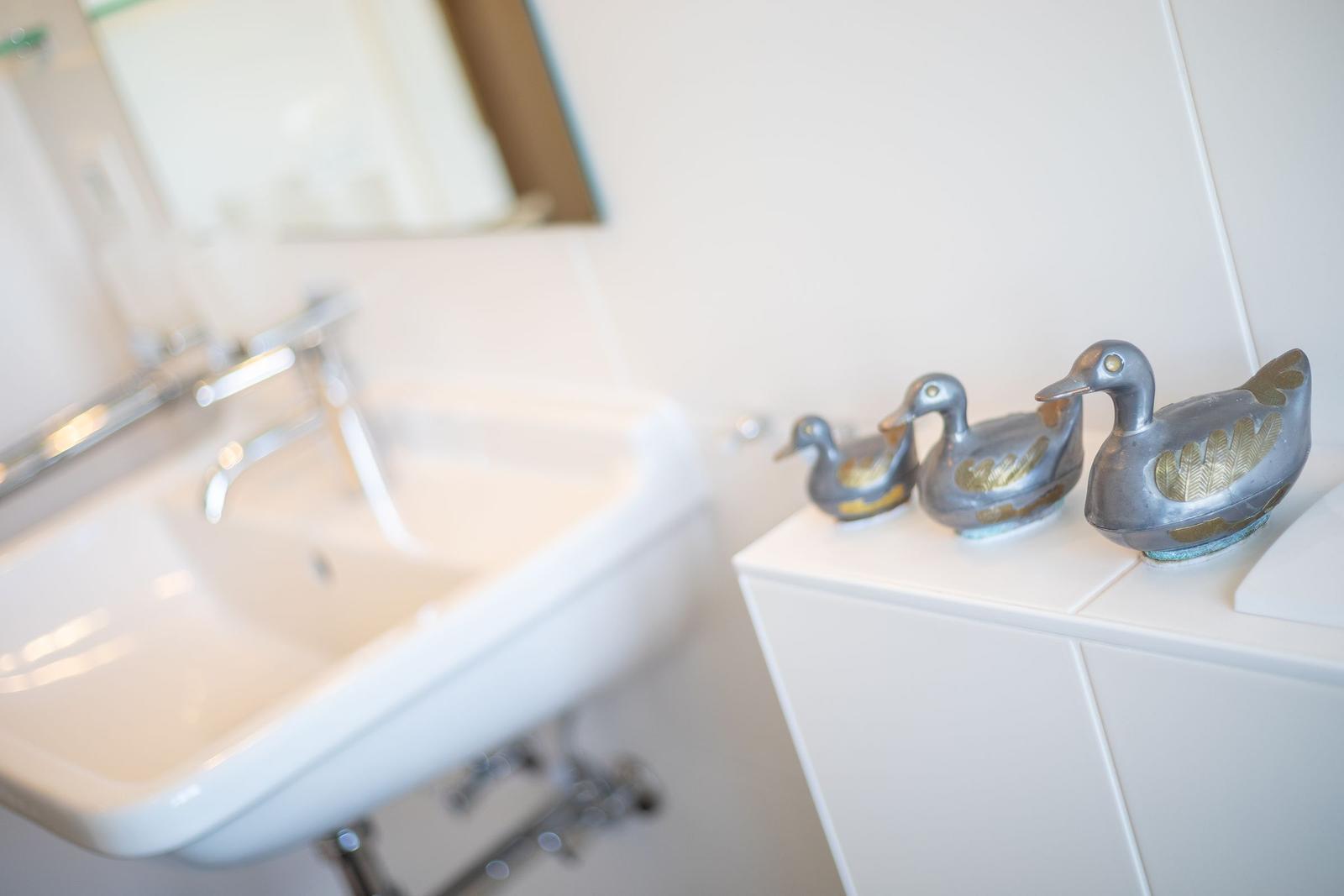 Badezimmer mit Waschbecken und drei dekorativen Entenfiguren auf Schrank.