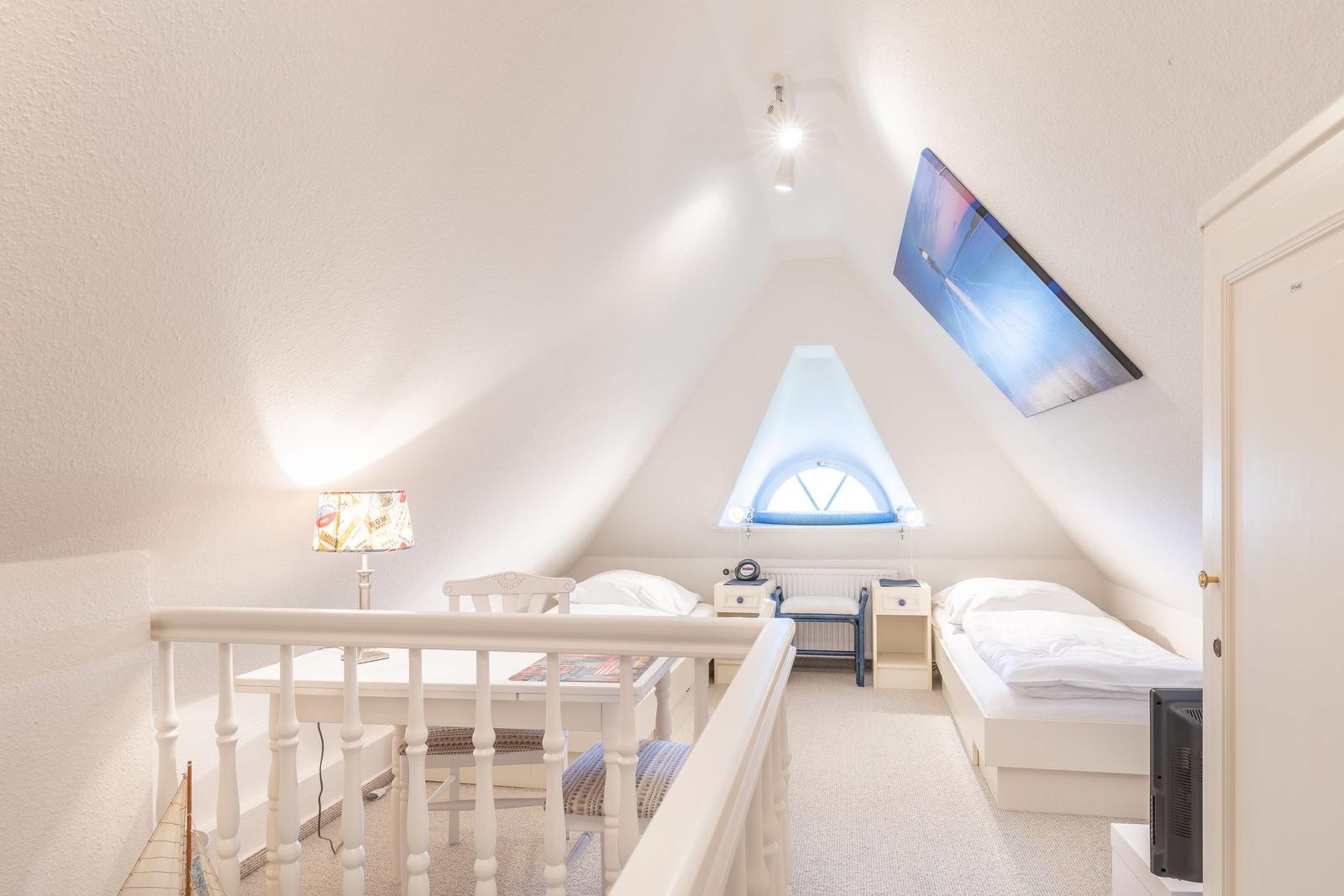 Zimmer mit Dachschrägen, Bett, Schreibtisch und Fernseher.