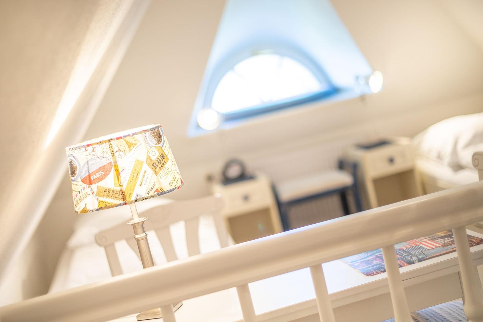 Schlafzimmer mit Dachschräge, Fenster und Lampe mit Briefmarkenmotiv.