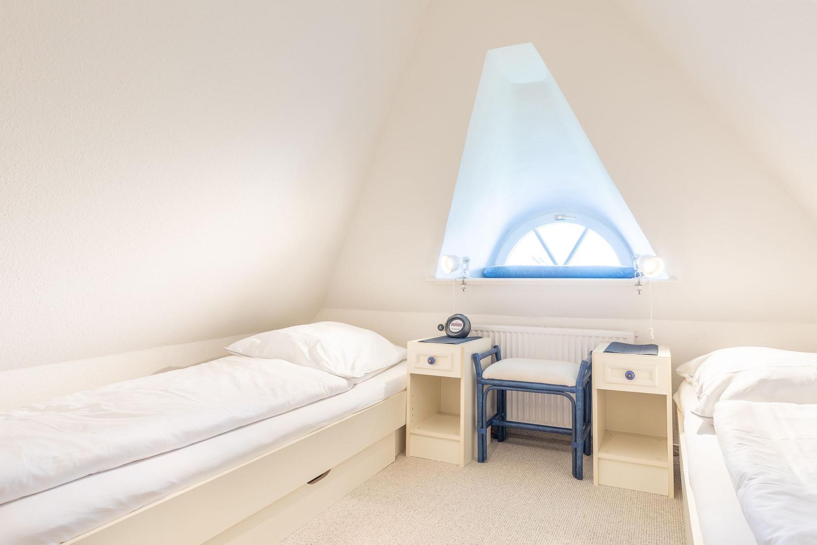 Zimmer mit zwei Betten, Schreibtisch und Dachfenster mit blauem Vorhang.