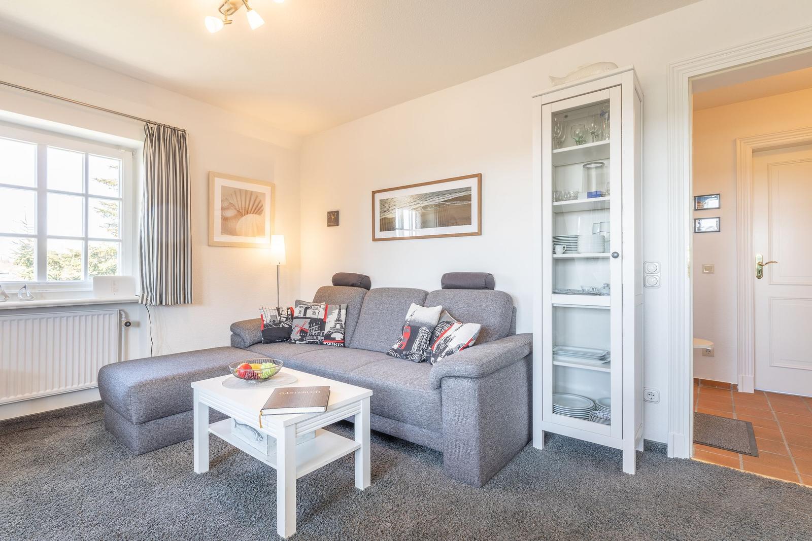 Wohnzimmer mit grauem Sofa, weißem Couchtisch und Glasvitrine.
