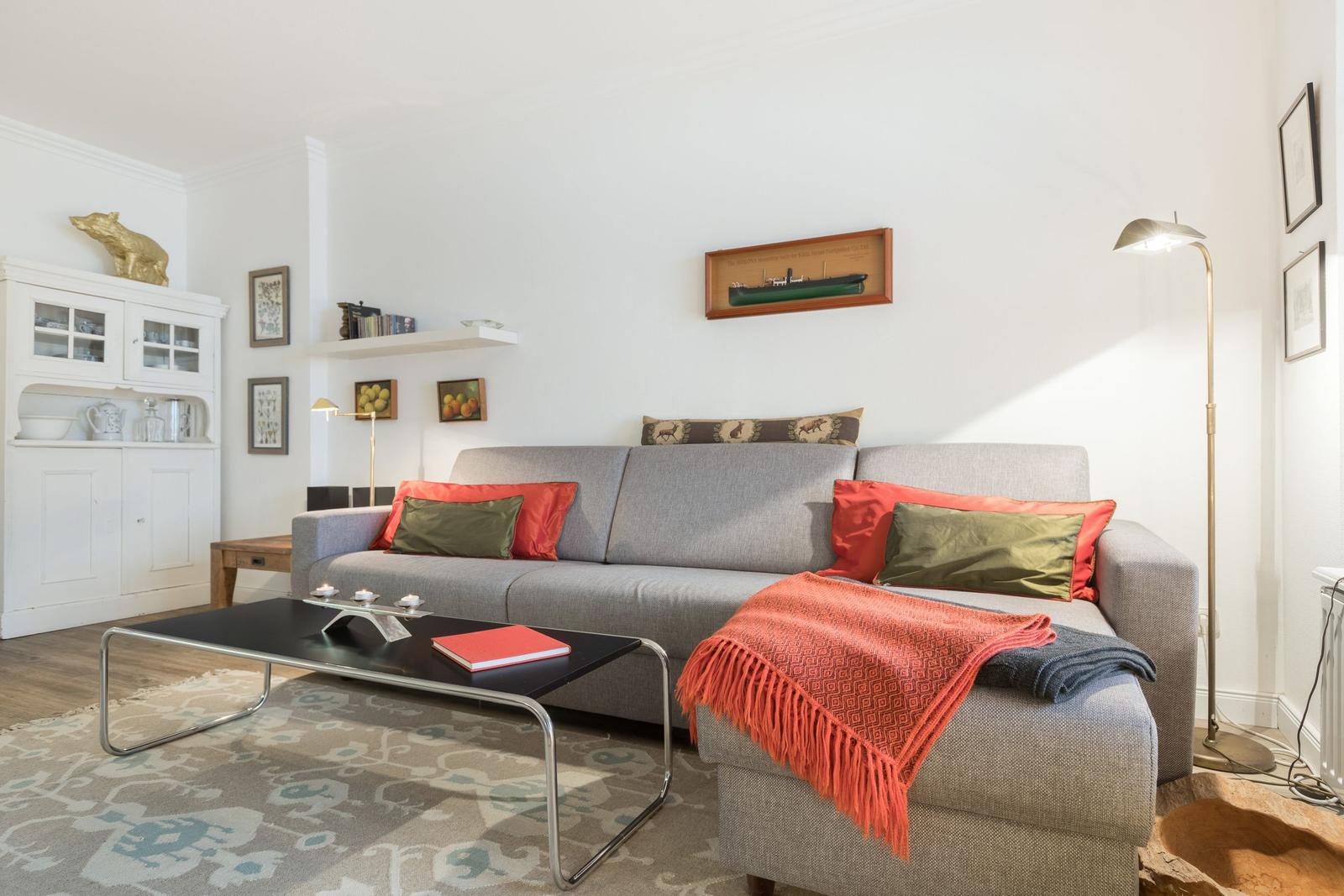 Ein Wohnzimmer mit grauem Sofa, rotem Decken und schwarzer Couchtisch.