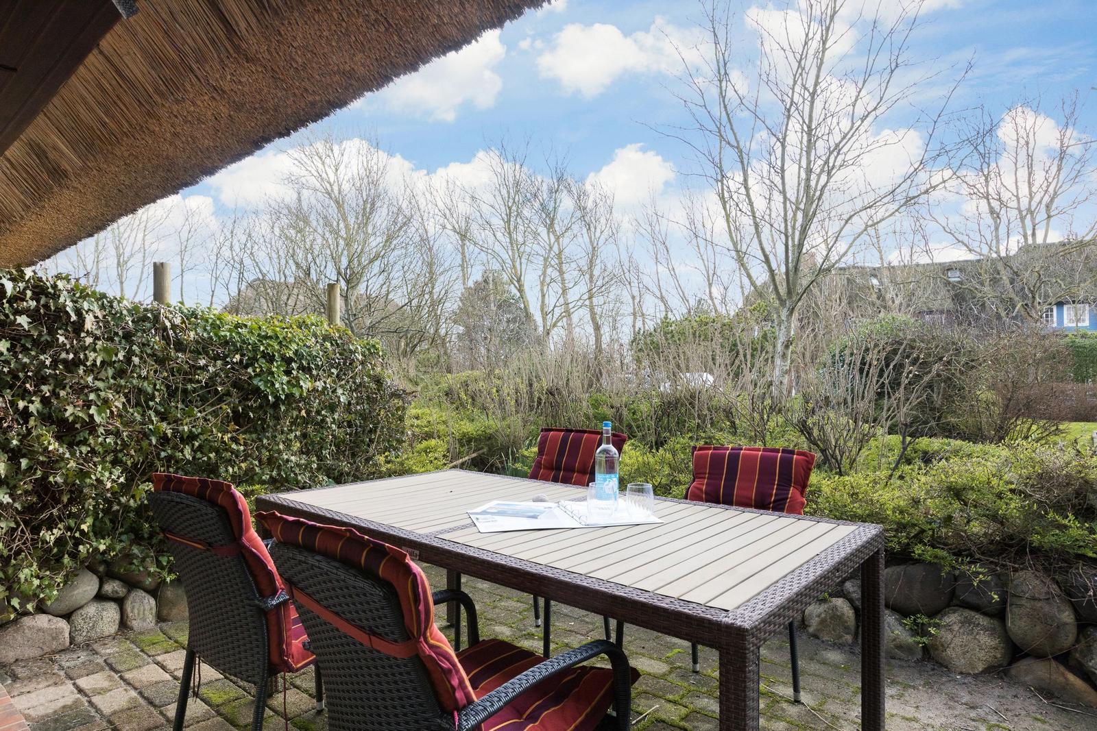 Terrasse mit Tisch und Stühlen unter strohgedecktem Dach.