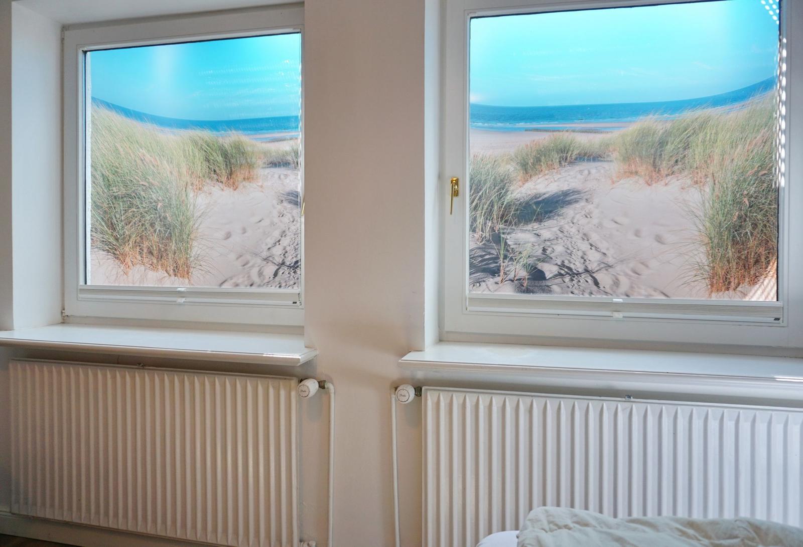 Zwei Fenster mit Blick auf Strand und Dünen.