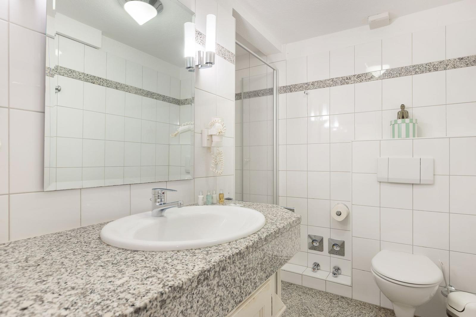Badezimmer mit Waschbecken, Spiegel, Dusche und Toilette.