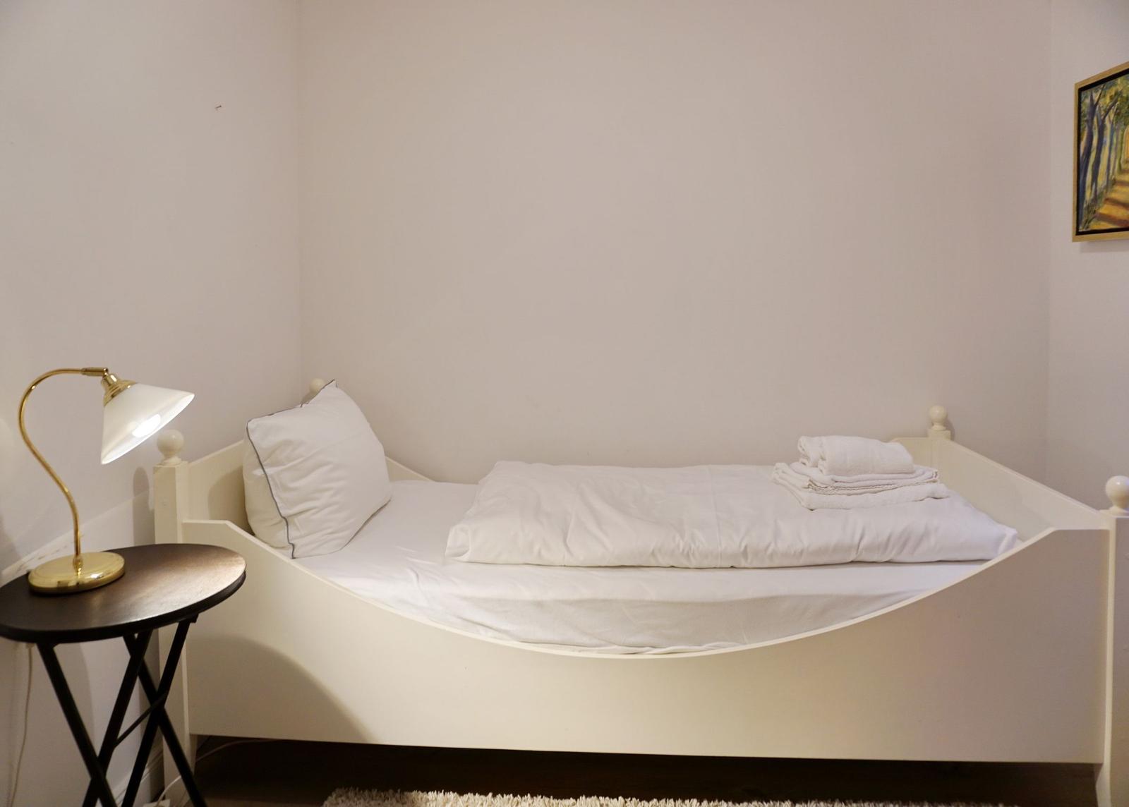 Ein Bett mit weißer Bettwäsche und Handtüchern, daneben ein Nachttisch mit Lampe.
