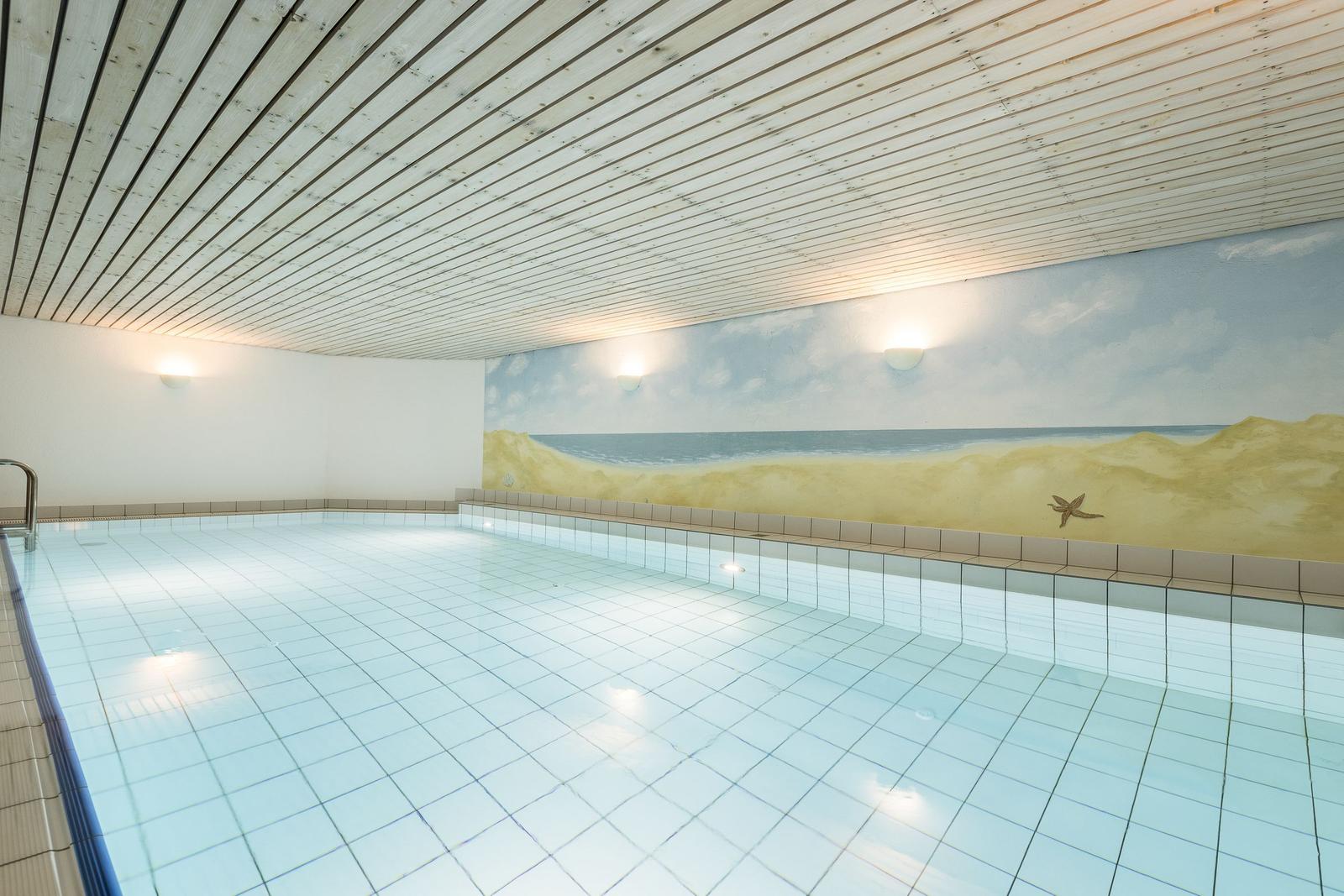 Innenpool mit Strandmotiv an der Wand und Holzdecke.