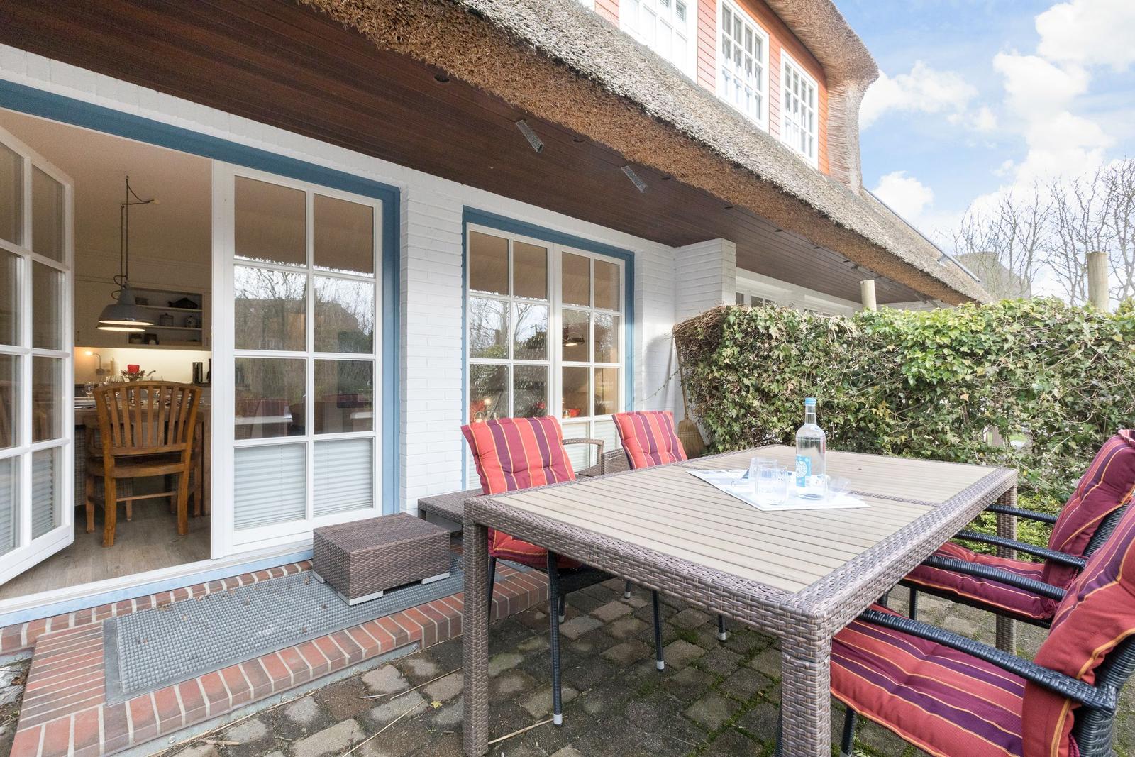 Terrasse mit Tisch und Stühlen vor einem Haus mit Dach aus Stroh
