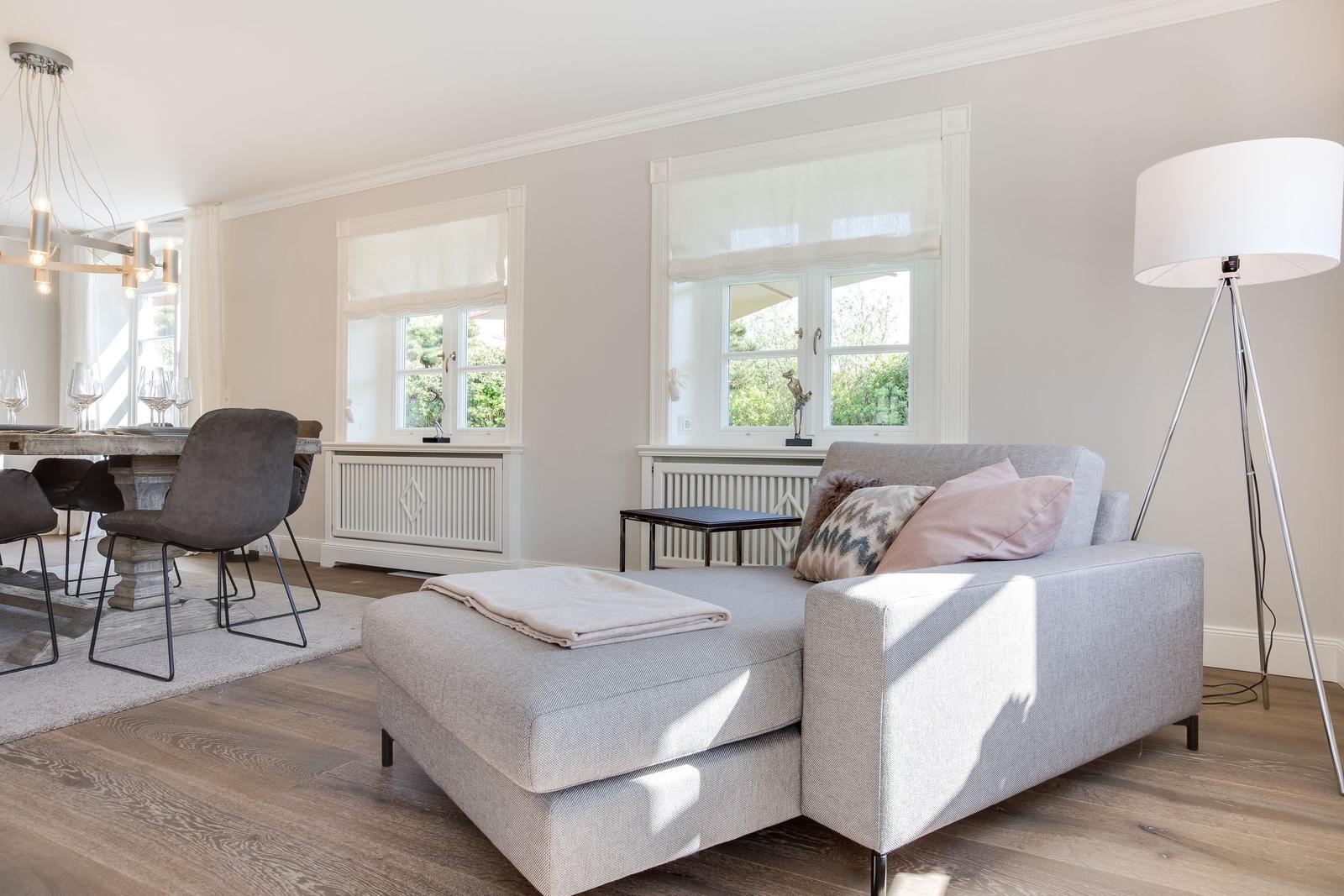 Wohn- und Essbereich mit Sofa, Tisch und Stühlen sowie Fenstern.