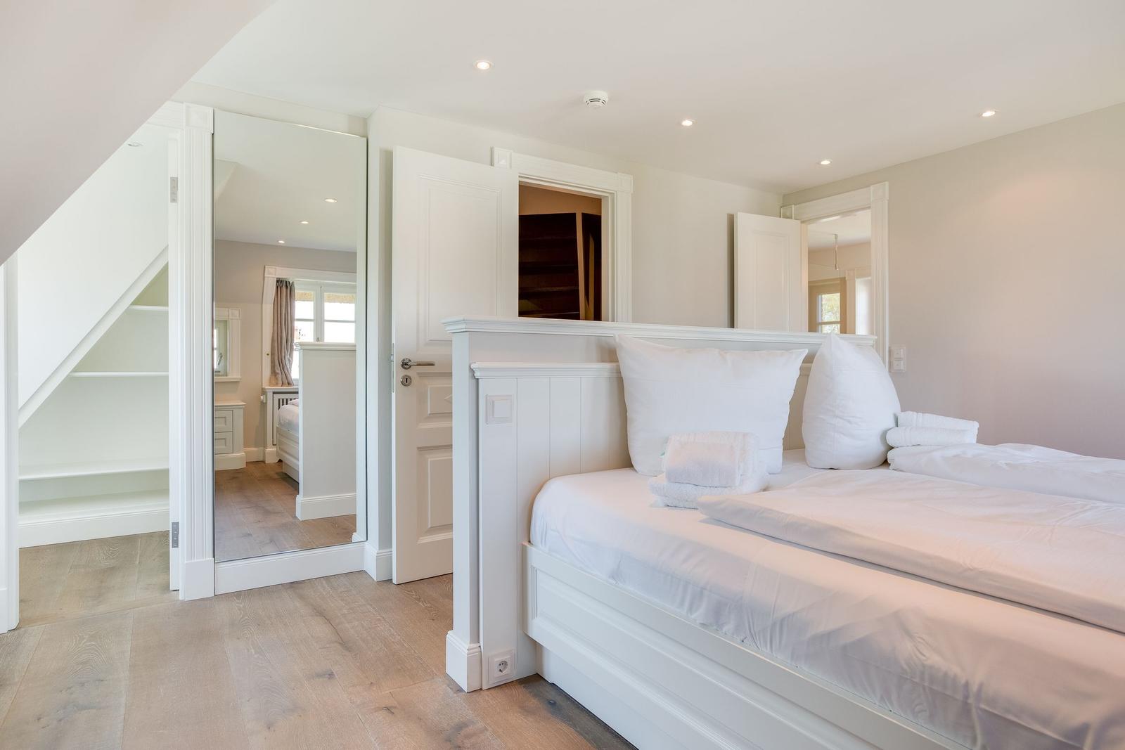 Schlafzimmer mit weißem Bett, Holzboden und Blick in angrenzende Räume.