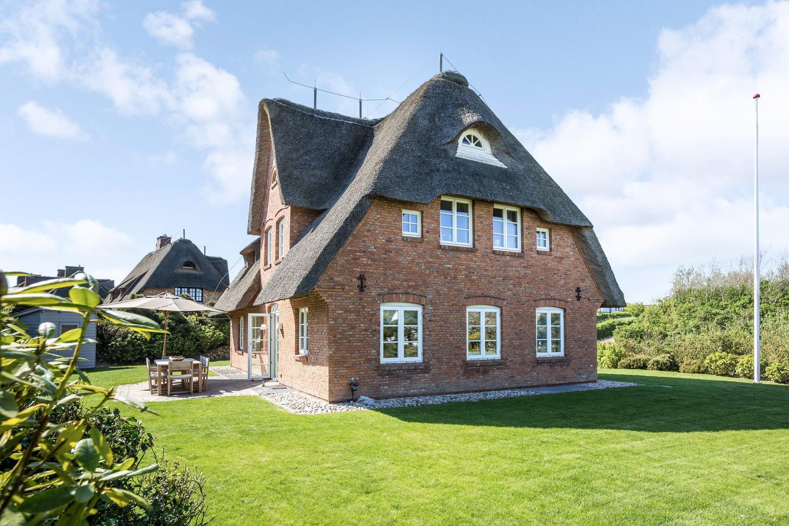 Rotes Backsteinhaus mit Strohdach und Gartenbereich mit Tisch und Stühlen.