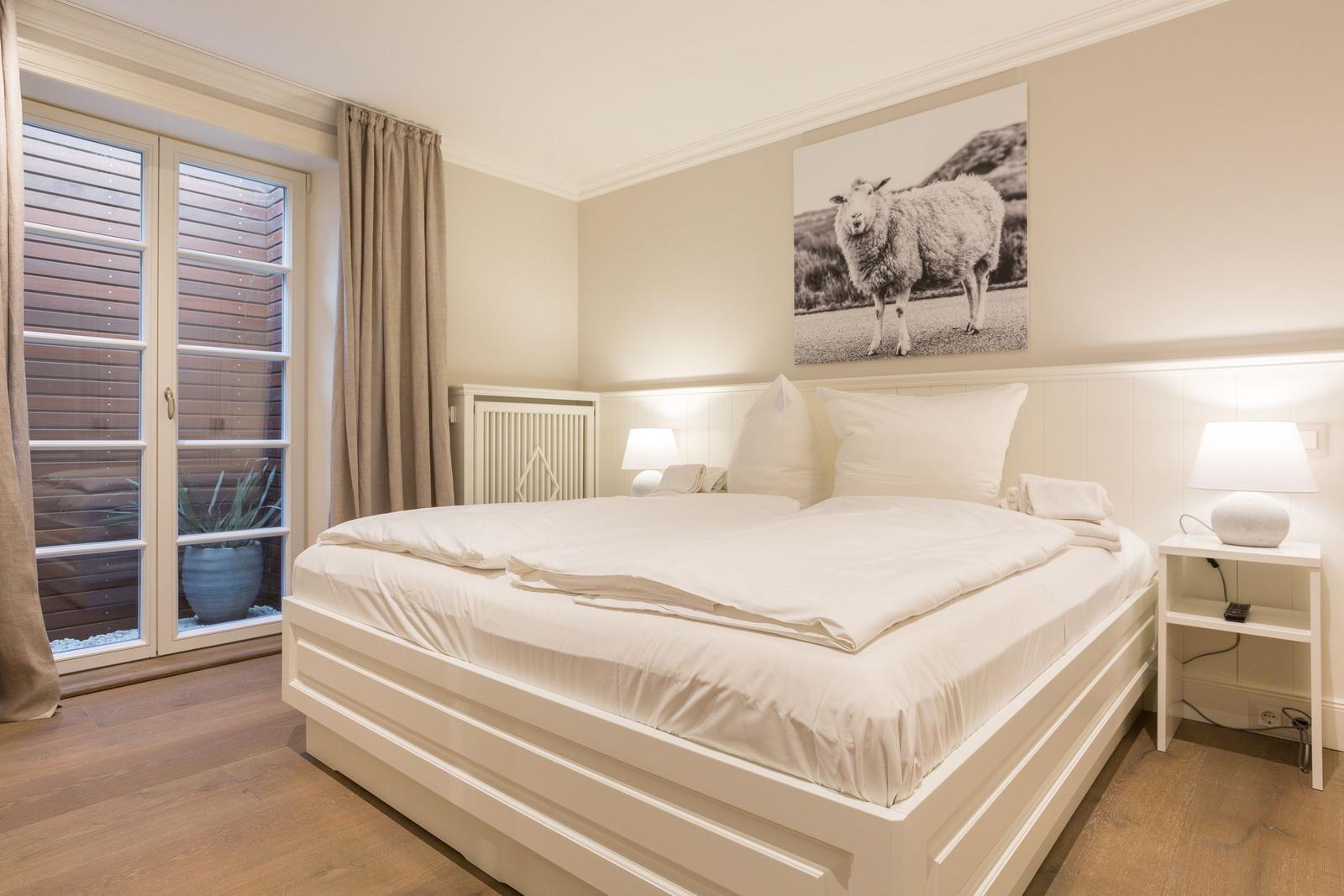 Schlafzimmer mit Doppelbett, Wandbild eines Schafs und bodentiefen Fenstern.