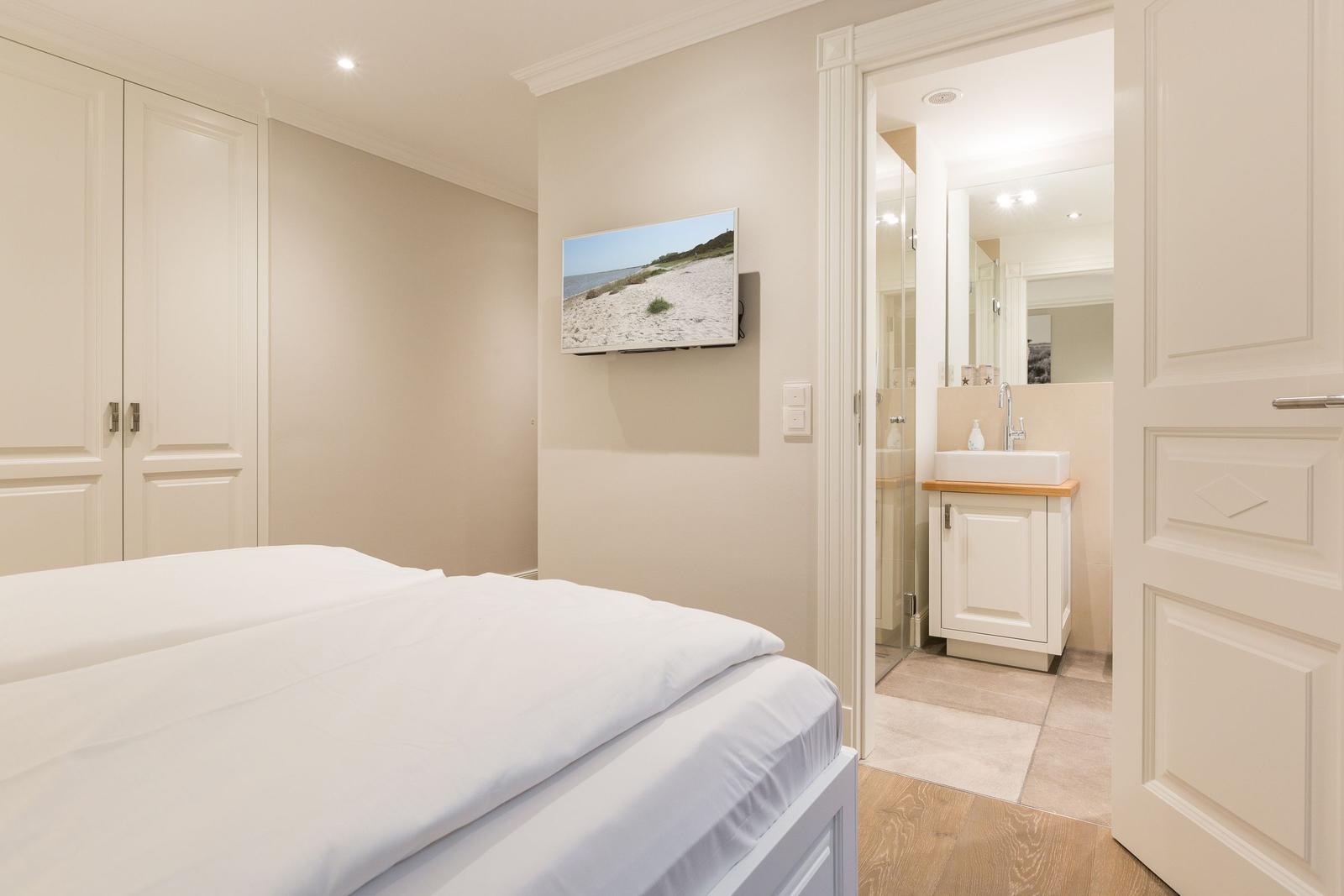 Schlafzimmer mit Bett, Kleiderschrank und TV. Angeschlossen befindet sich ein Badezimmer.