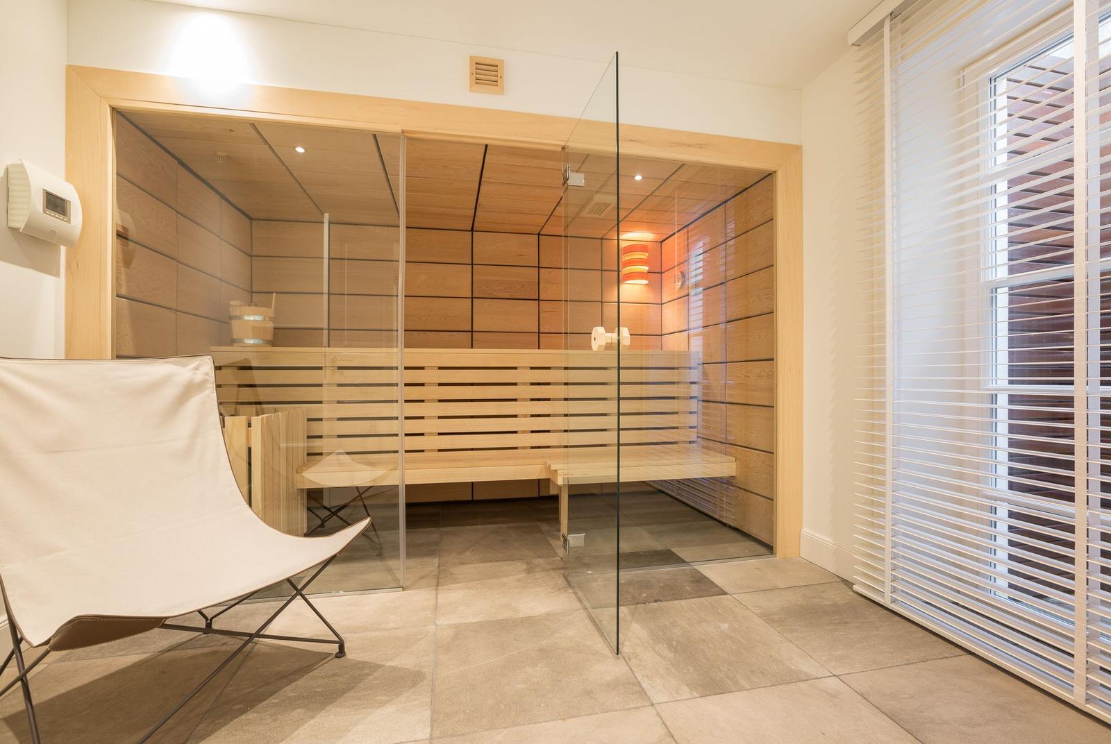 Sauna mit Glaswand, Holzbank und Fenster mit Jalousie.