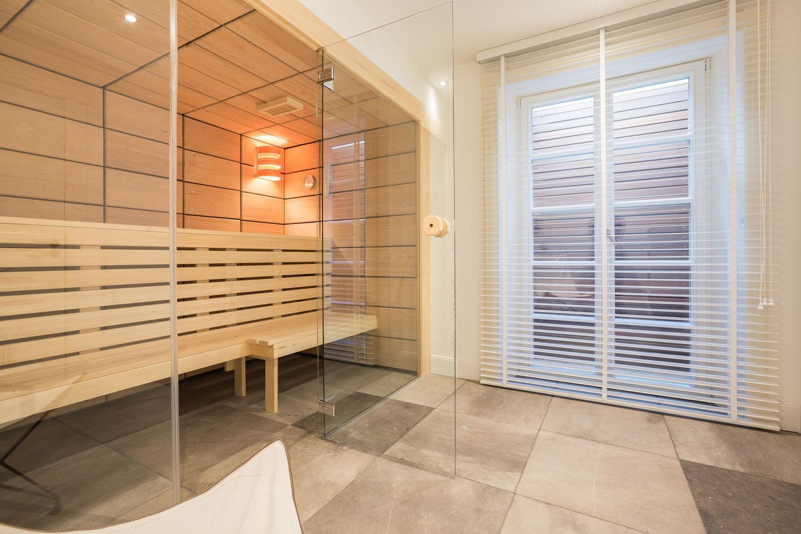 Sauna mit Holzwand und Glasabtrennung, daneben Fenster mit Jalousie.