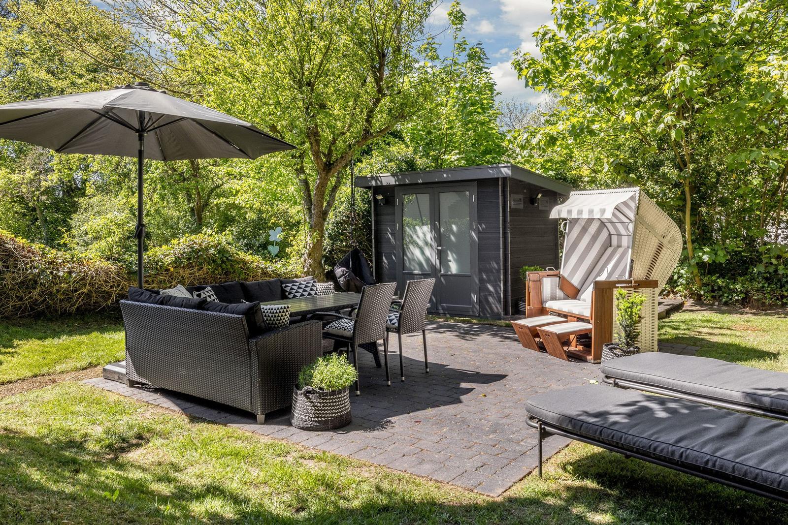 Terrasse mit Sitzgruppe, Sonnenschirm und Liegestühlen um einen Gartenhaus.