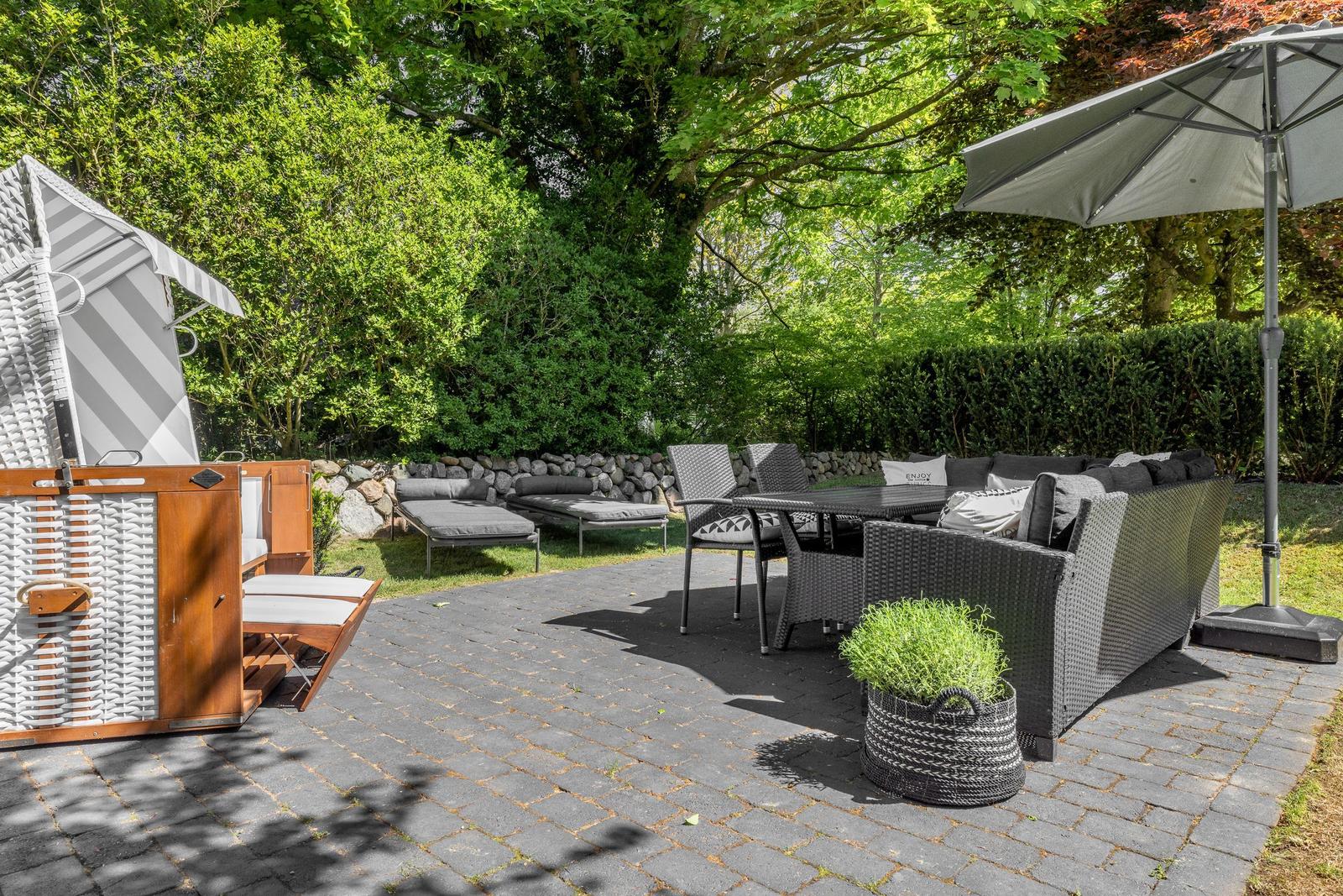 Terrasse mit Sitzgruppe, Sonnenschirm und Liegestühlen. Umgeben von Bäumen und Sträuchern.