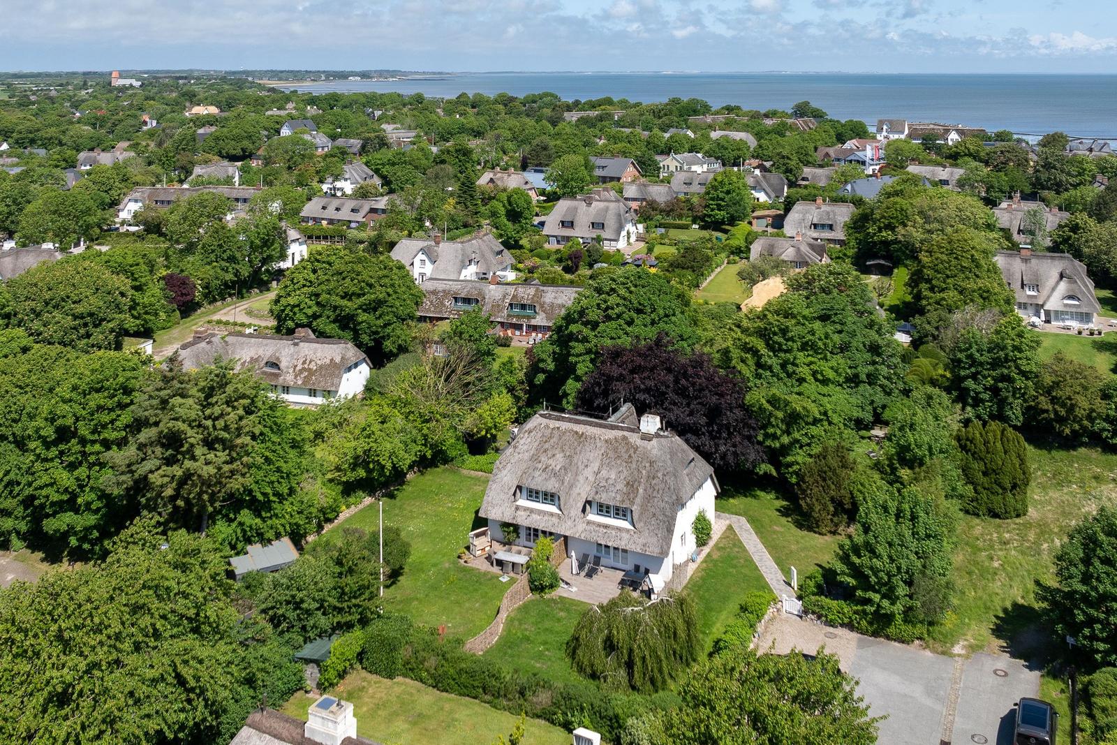 Dorfhaus mit Strohdach und Garten. Blick auf Meer und grüne Landschaft.