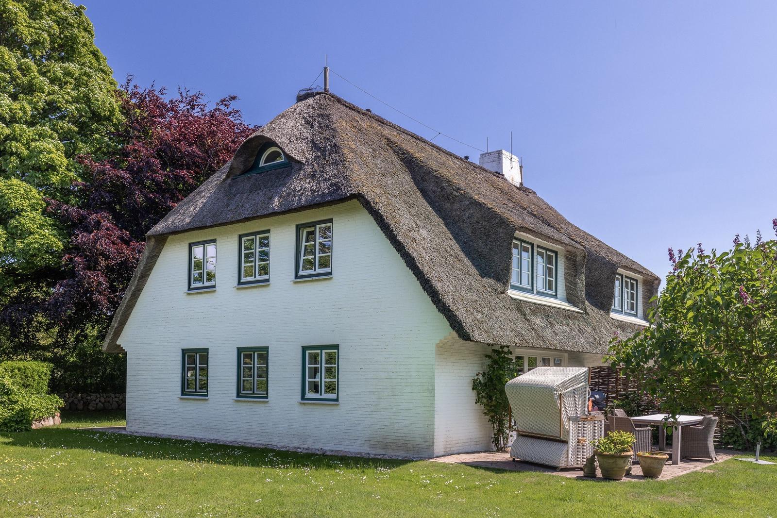 Ein weißes Haus mit Strohdach, Fenstern und einer Terrasse im Garten.